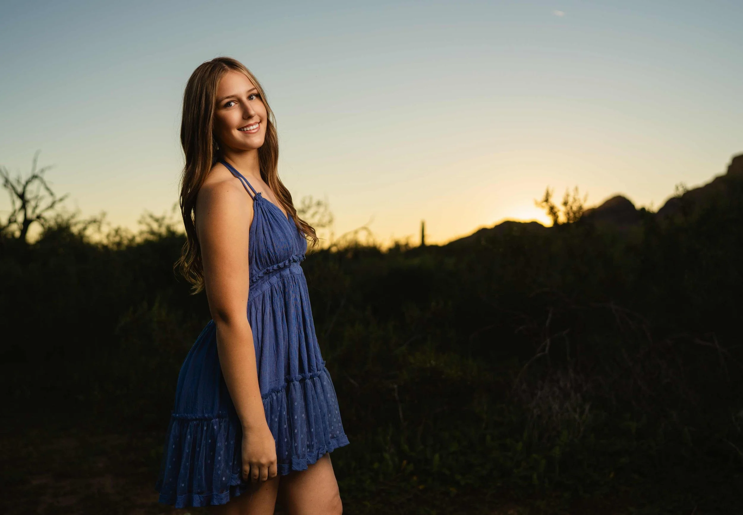 A high school senior from Phoenix striking a pose in the desert with the sun setting behind her