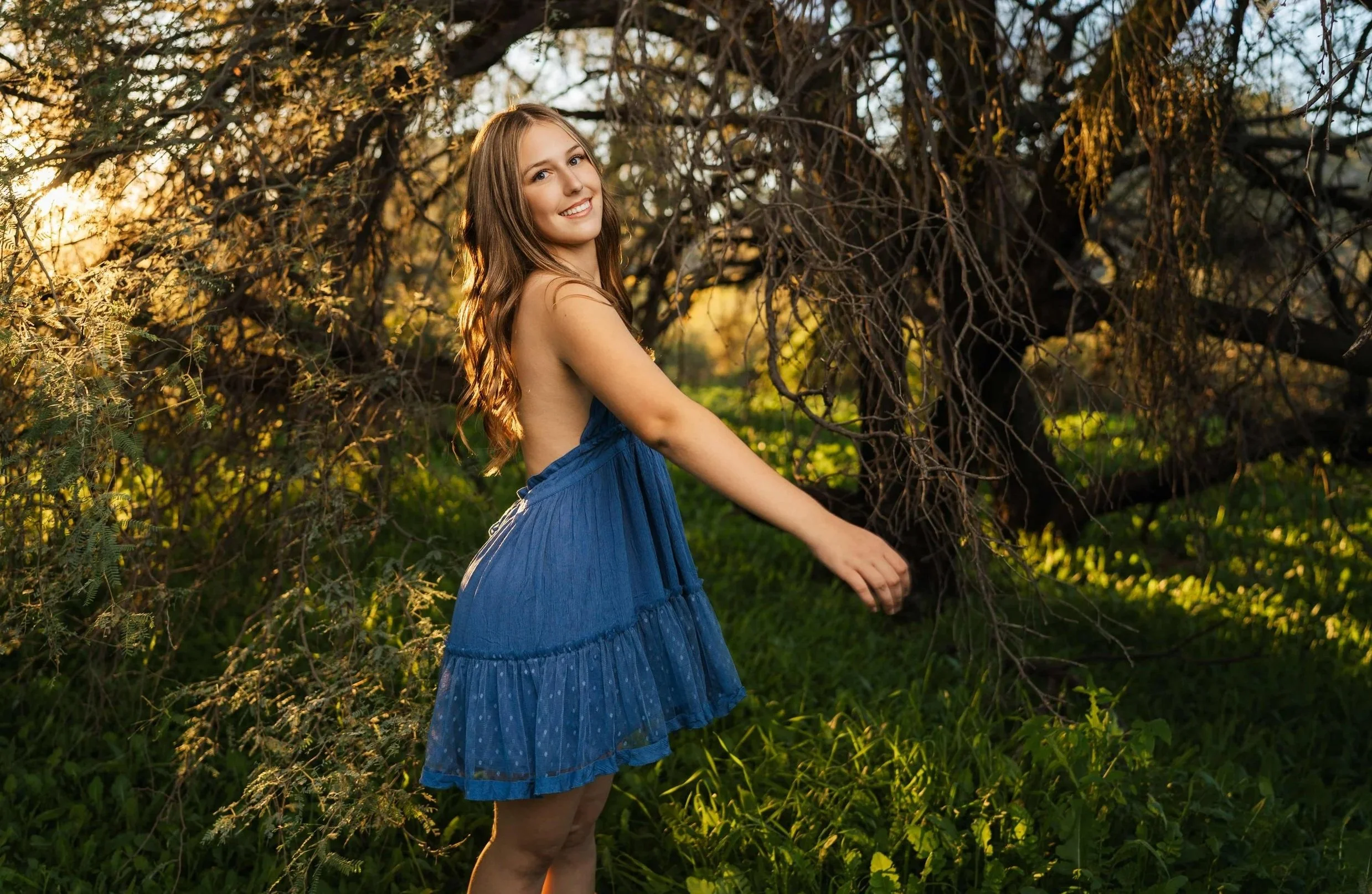 A young woman dancing in a field of green during her senior photoshoot in Phoenix