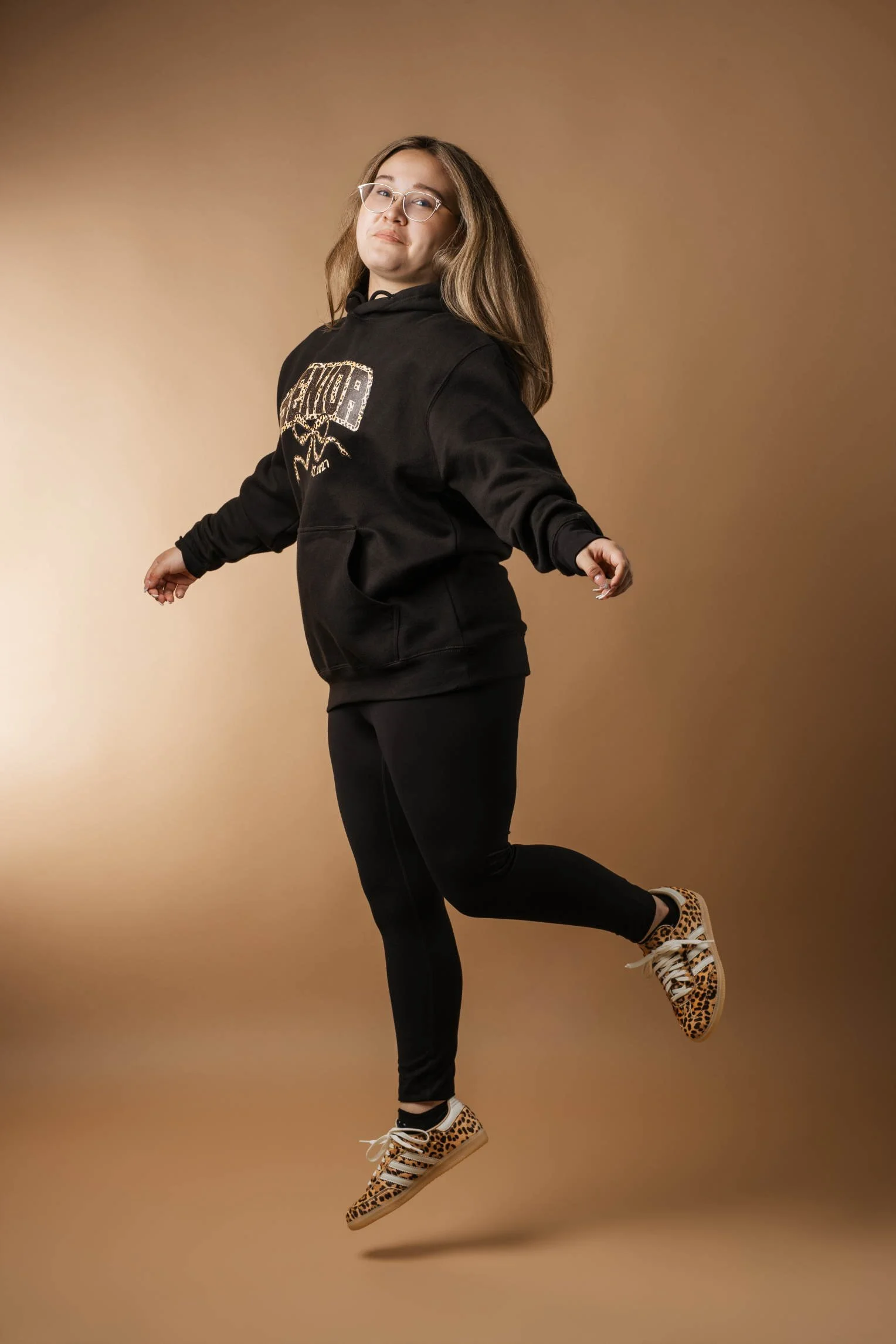 young woman in high school jumping in front of a mocha backdrop
