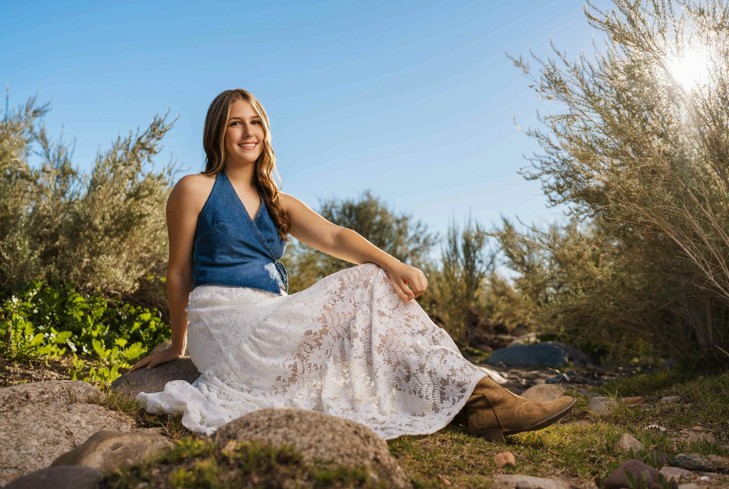 A senior from Phoenix sitting in a field of grass and bushes during her senior session at the Salt River