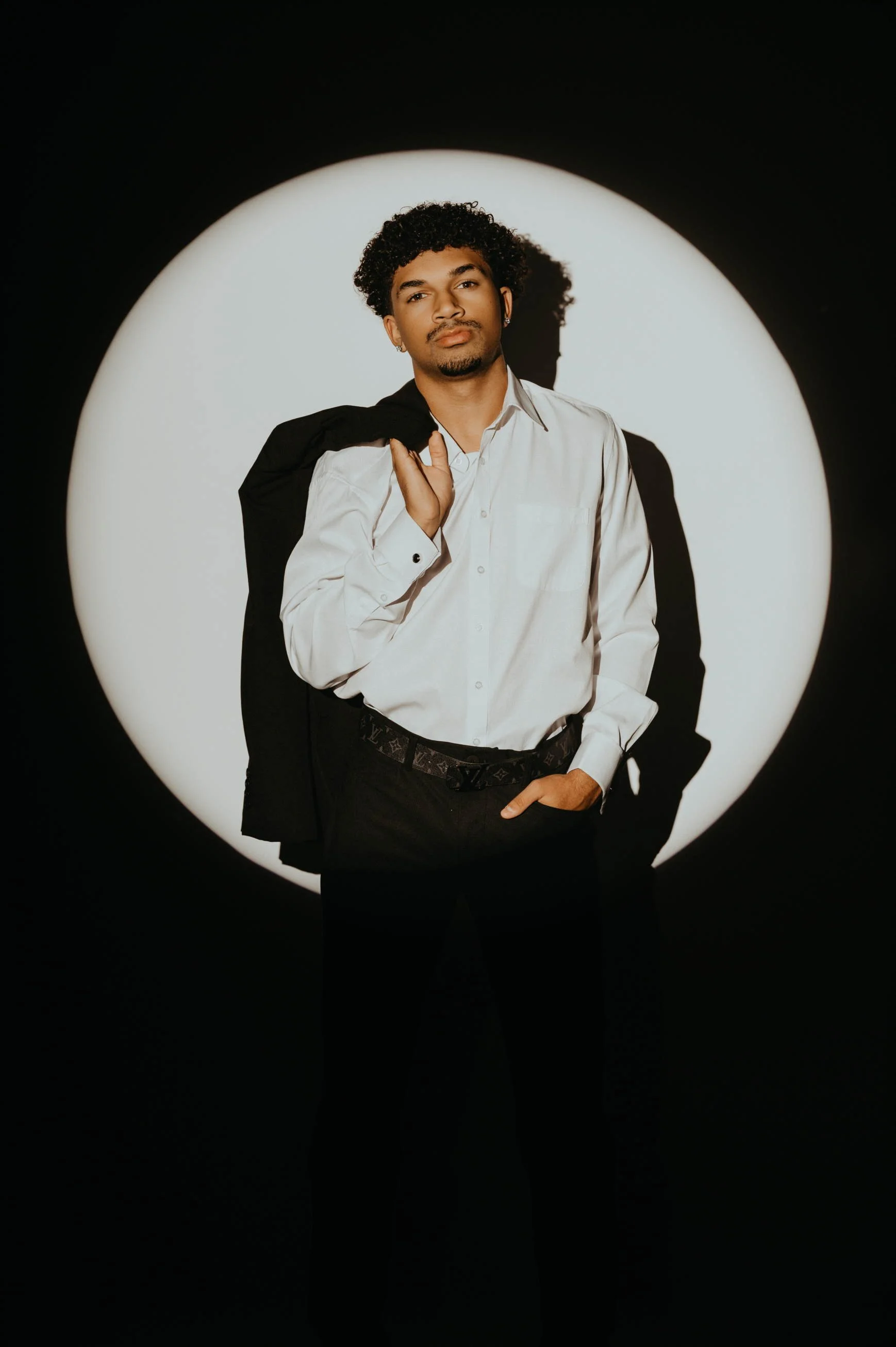 High school senior boy in Phoenix standing in front of a light with a jacket over his shoulder and hands in pocket