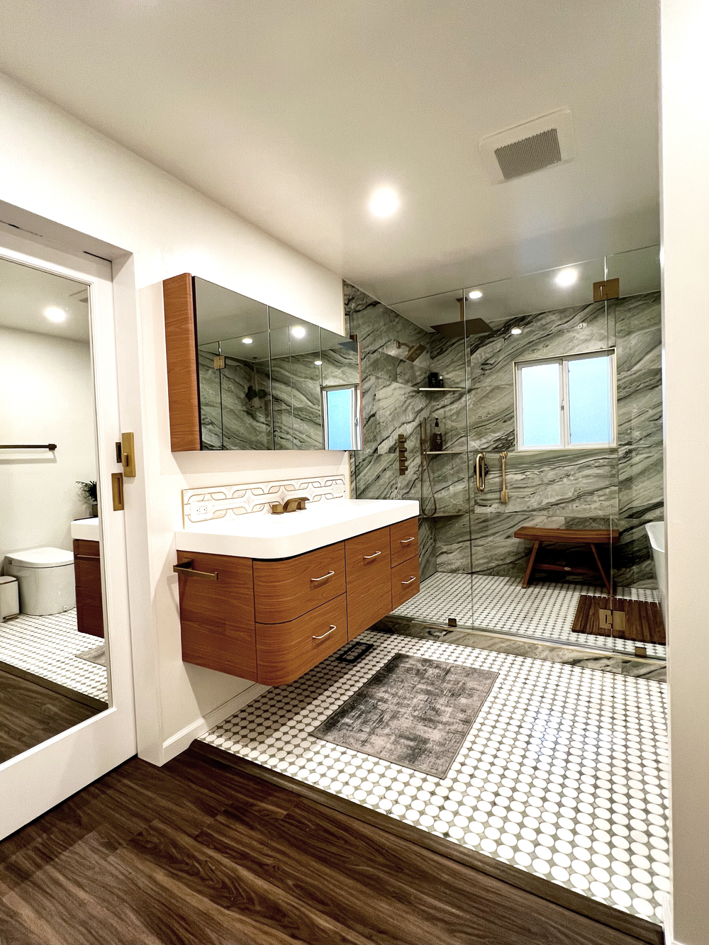Bathroom remodel with a wood vanity, white countertop, mirrored cabinet, marble wall and glass shower enclosure with a window