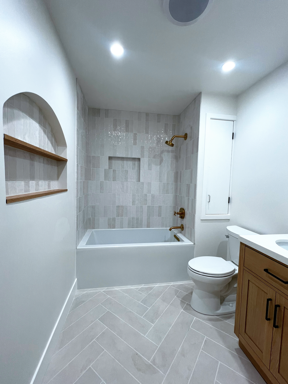 Bathroom remodel with a bathtub, gold fixtures, tiled shower area, wood vanity, built-in wall cabinet and light gray diagonal-pattern floor tile