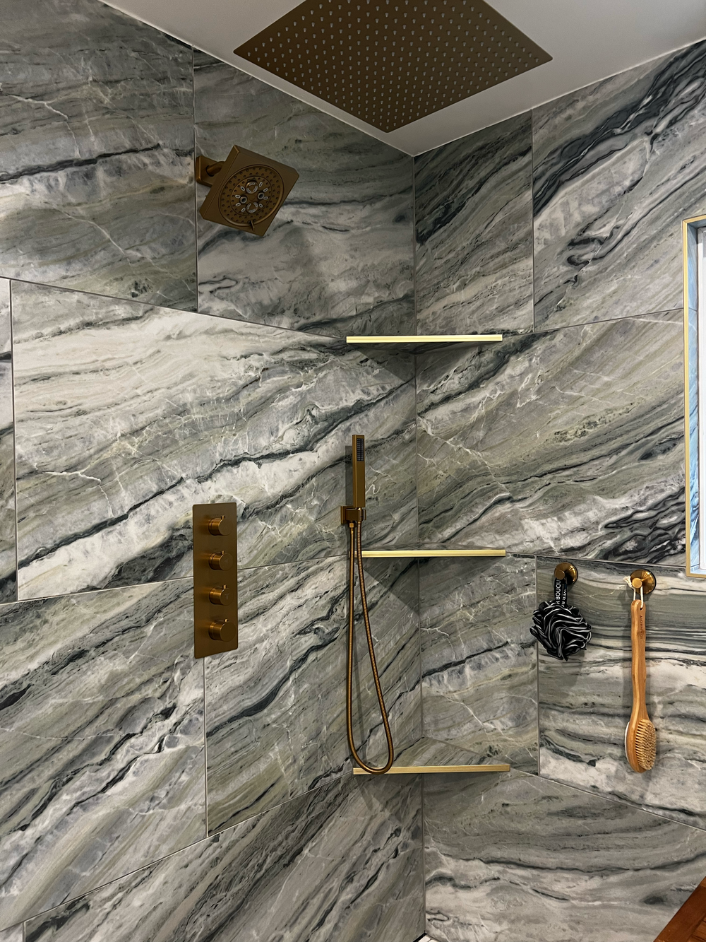 Shower remodel with marbled gray and white tile, gold showerhead, gold handheld shower wand and gold control panel