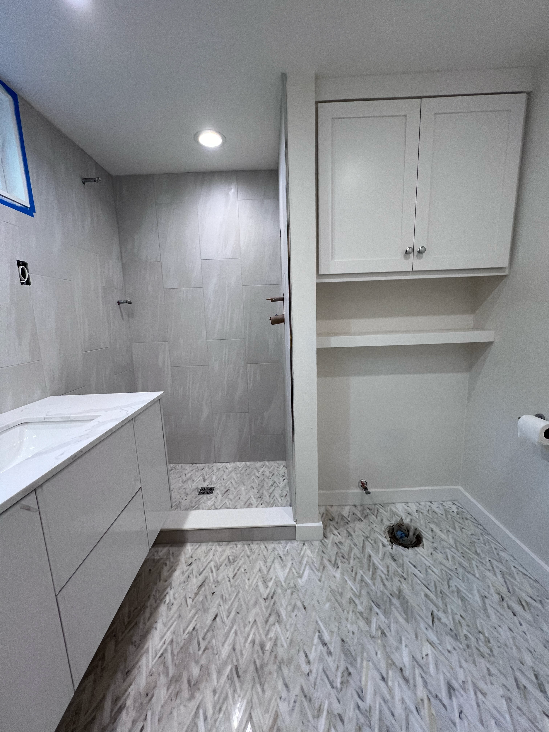 Bathroom under construction with wall tiles, cabinetry, and flooring installed, but fixtures not yet in place.