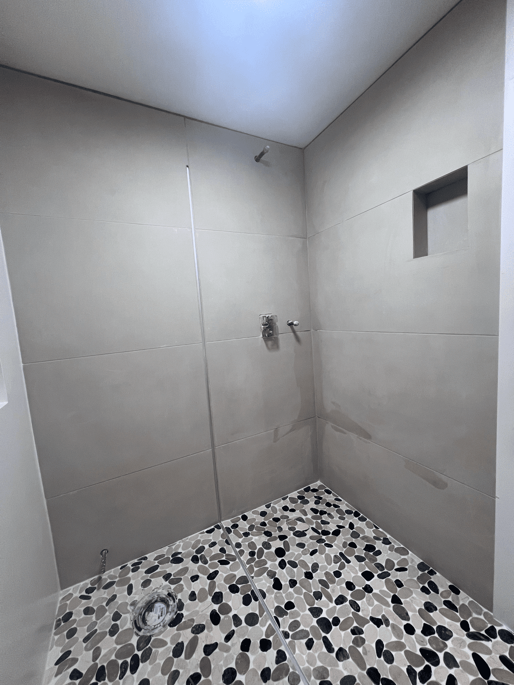 Walk-in shower remodel with beige tiled walls, a small wall niche and a pebble tile floor