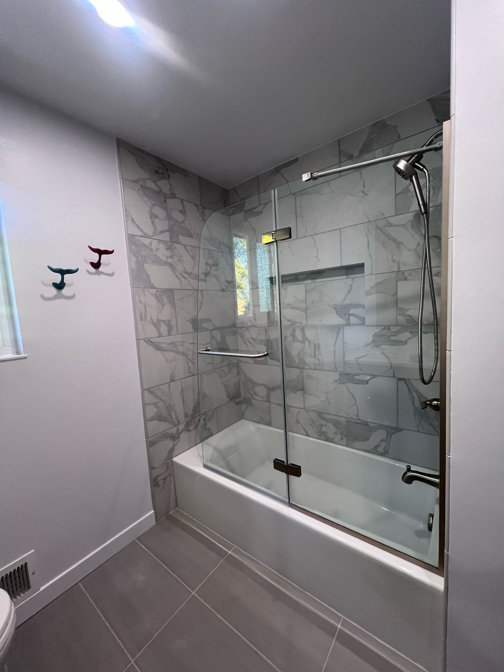 Bathroom remodel with a bathtub, glass shower enclosure, gray marble tile walls, dark gray floor tile and a window