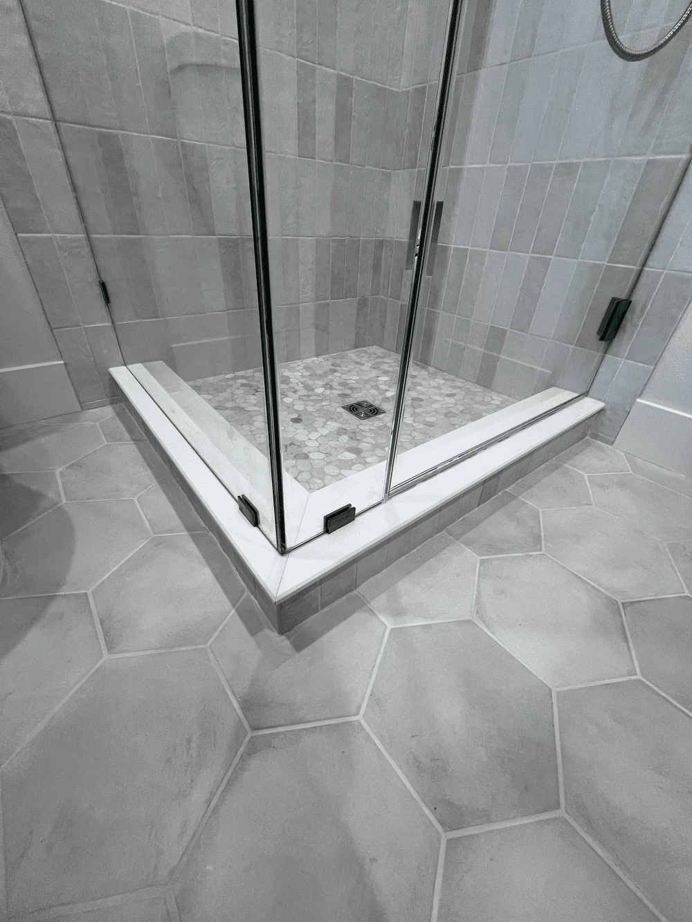 Shower remodel with a glass enclosure, metal handle and hinges, beige tiled walls and mosaic tile floor with a drain