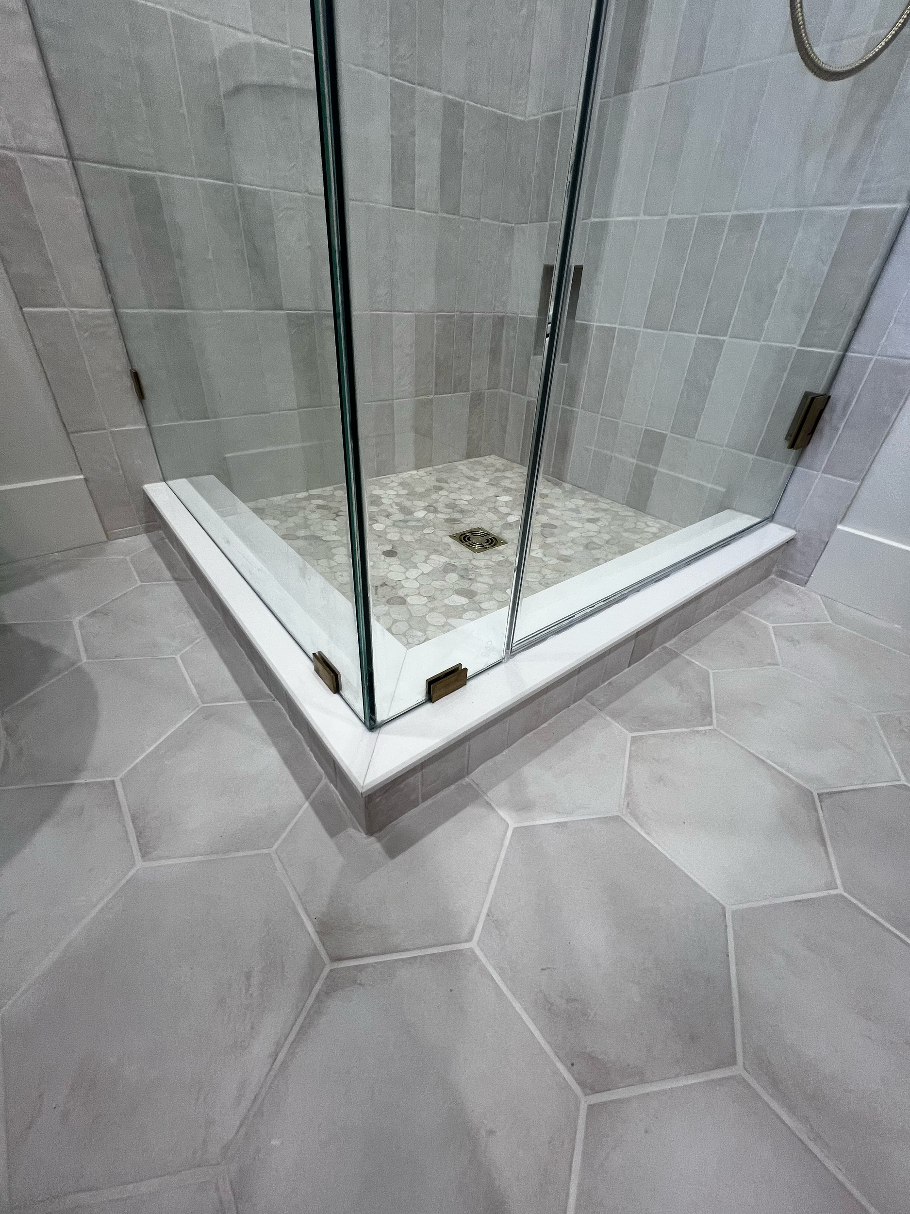 Shower remodel with a glass enclosure, metal handle and hinges, beige tiled walls and mosaic tile floor with a drain