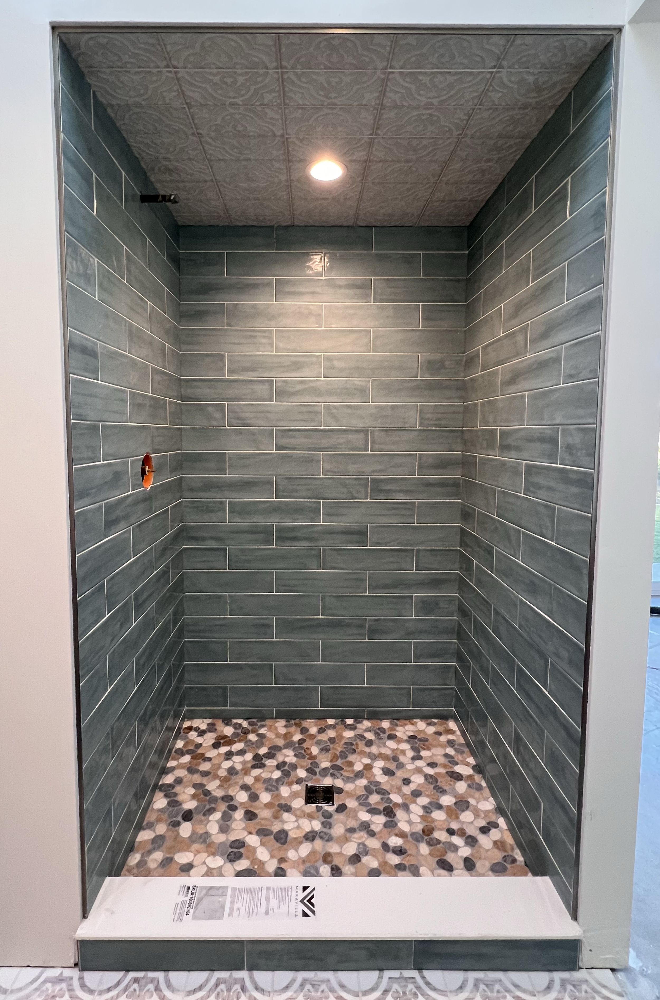 Walk-in shower remodel with teal subway tile walls, pebble tile floor, ceiling light and center drain