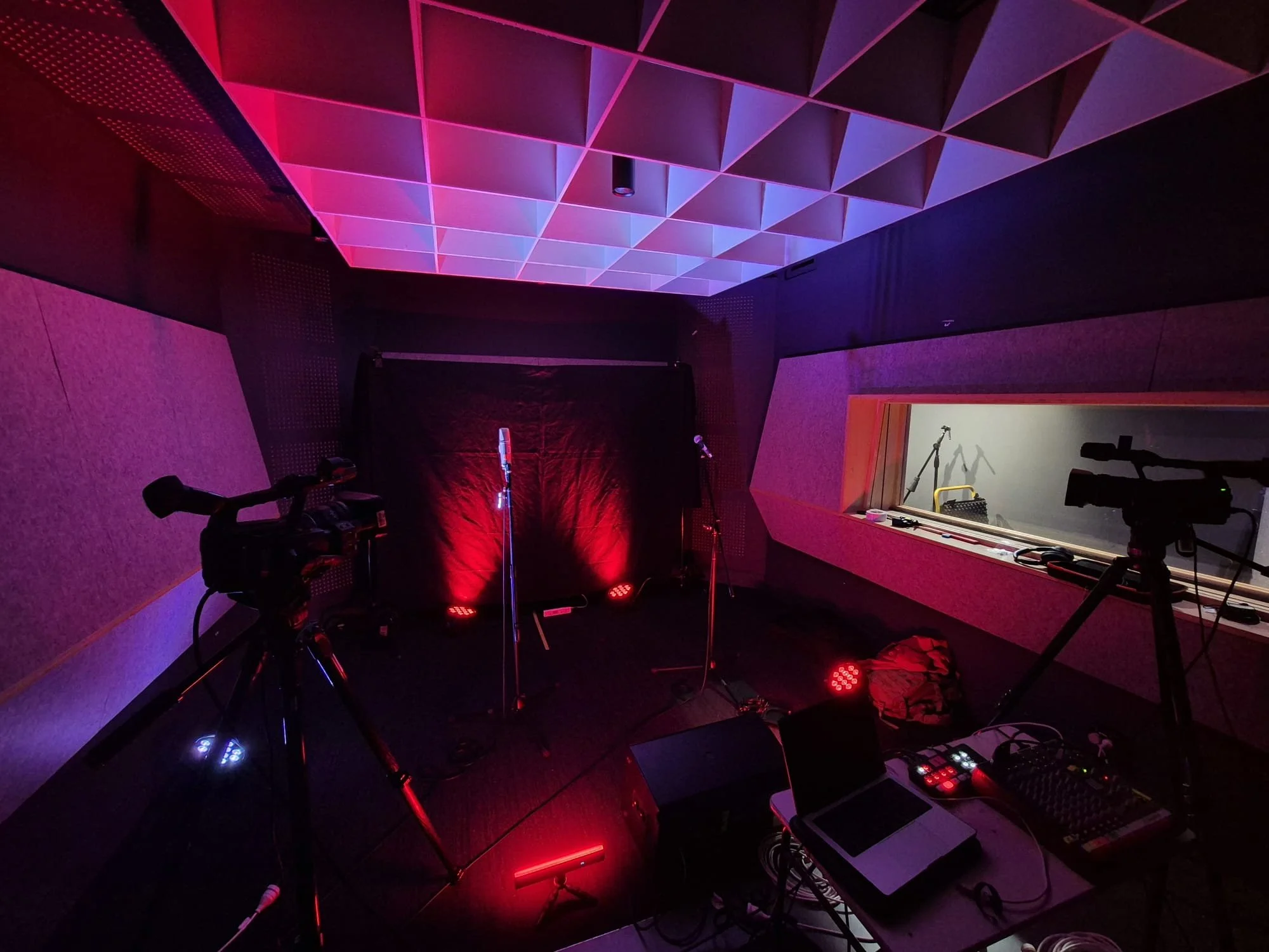 Recording studio with microphones, cameras, and lighting equipment in a dimly lit room with purple and red lighting.