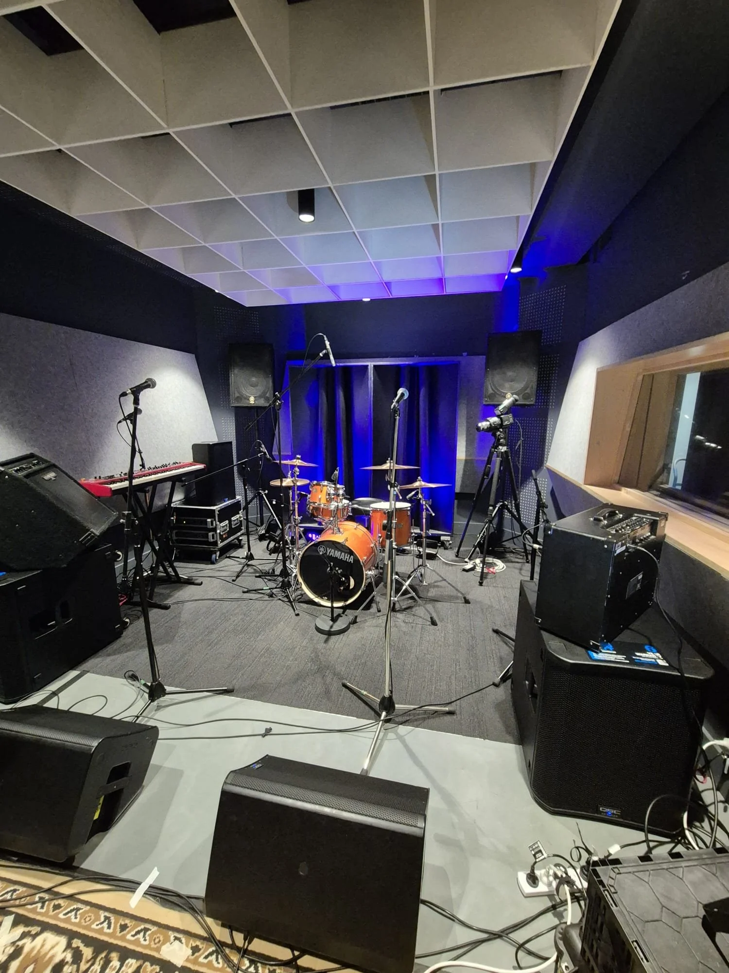 Music performance stage with drums, keyboard, microphones, speakers, and camera in a recording studio