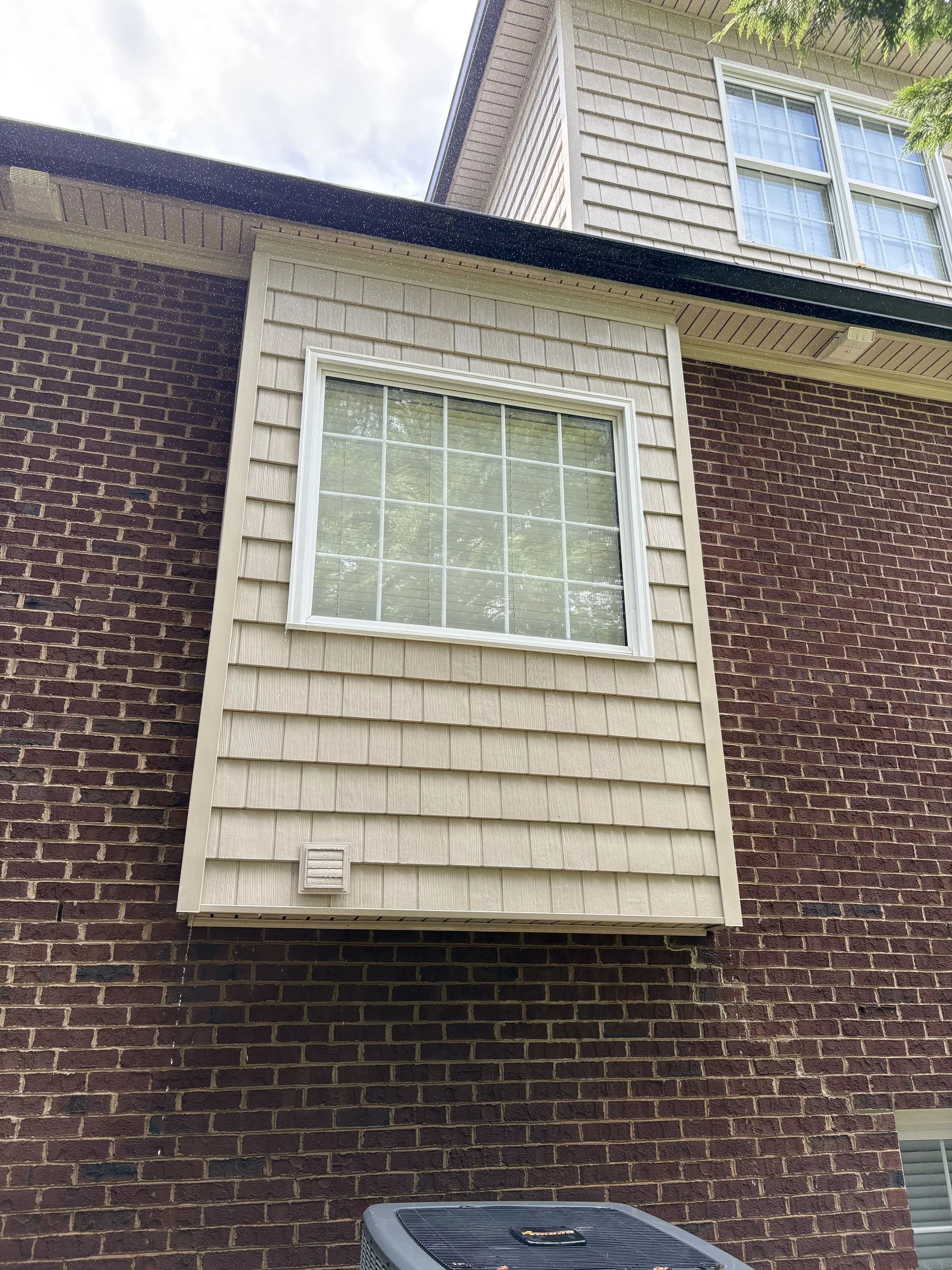 Exterior of a brick house with a white window and beige siding section.