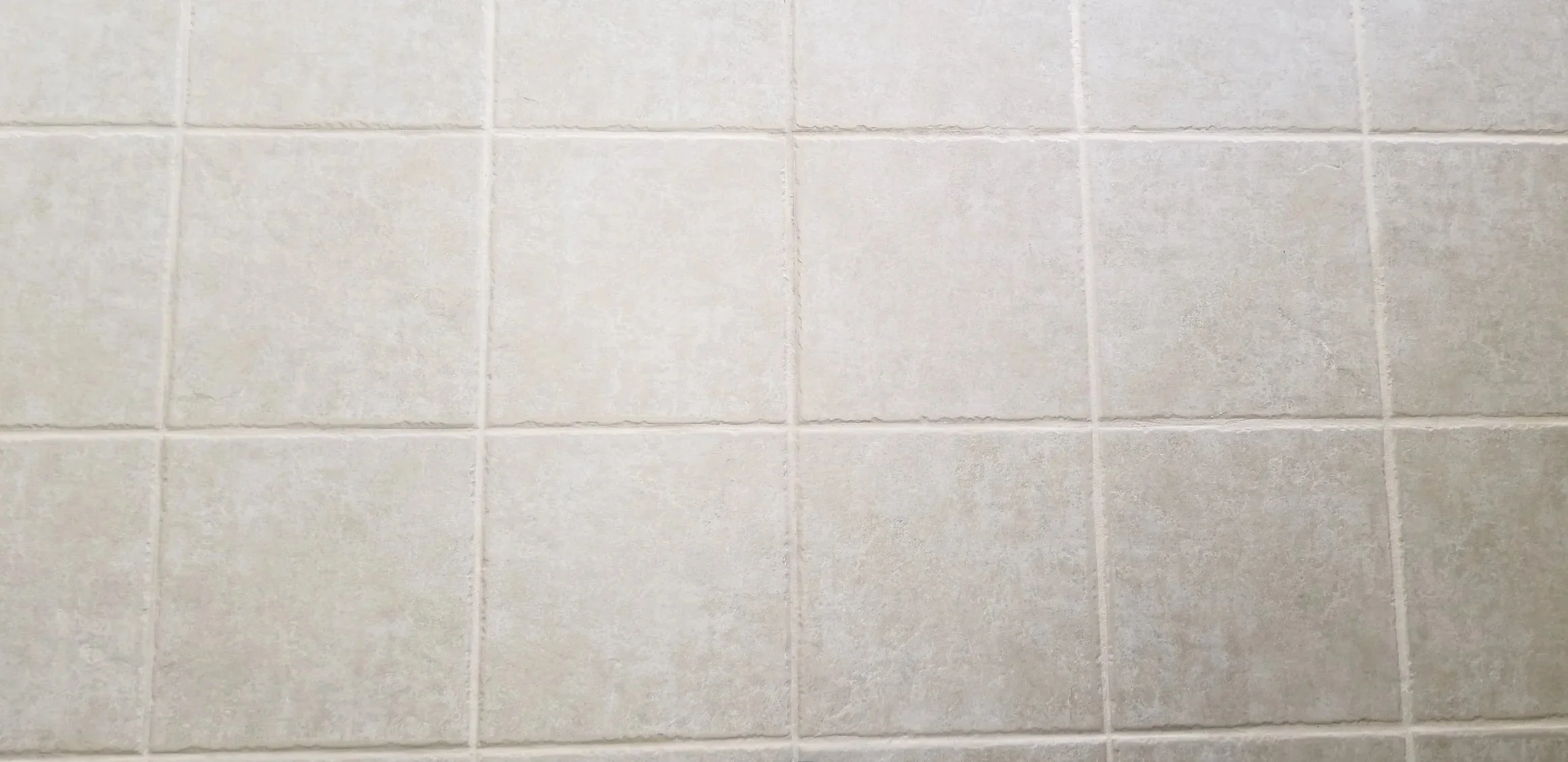 A close-up view of a tiled wall with light-colored square tiles and grout lines.