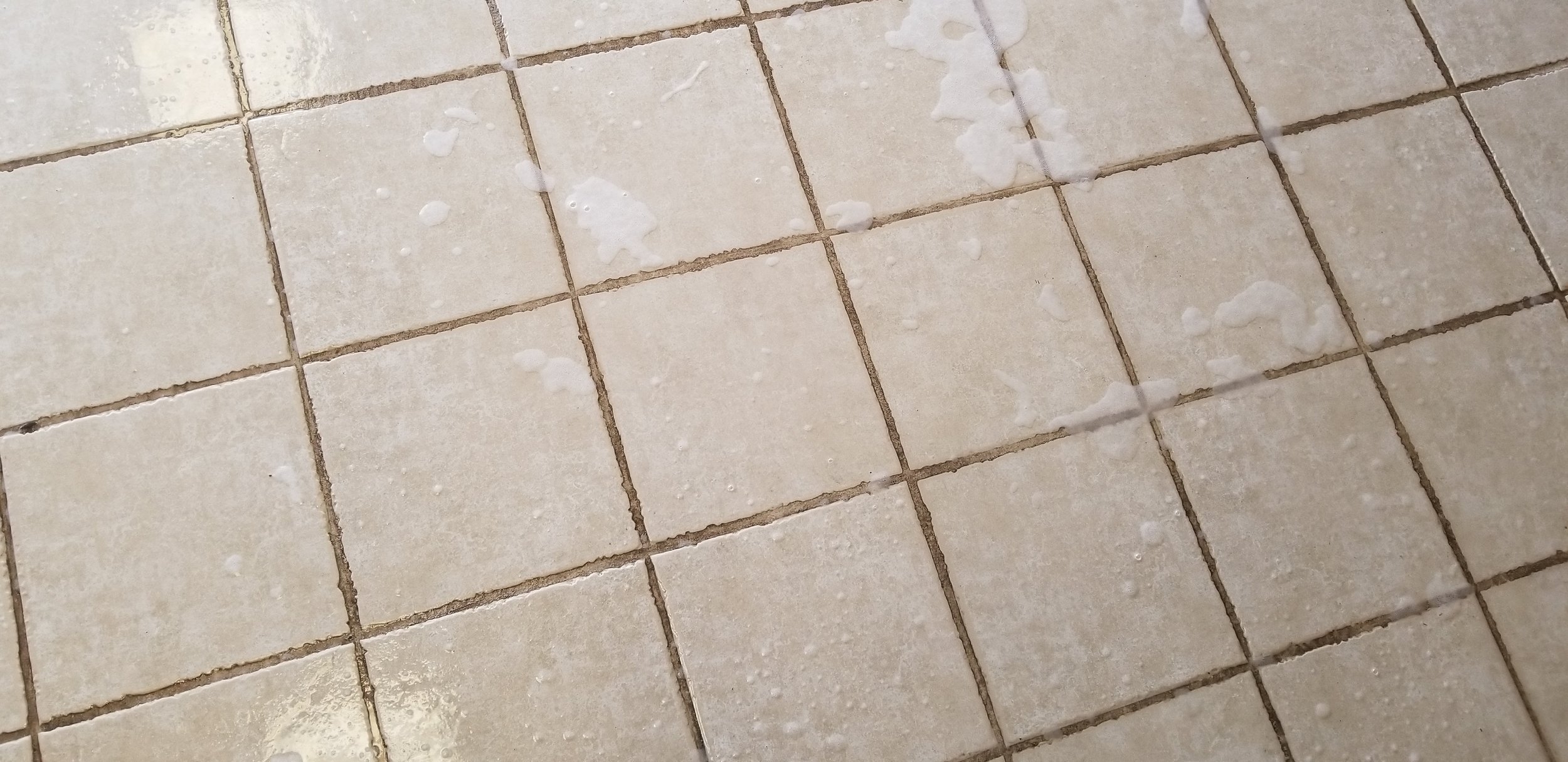 A tiled bathroom floor with soap or cleaning residue scattered across the tiles.