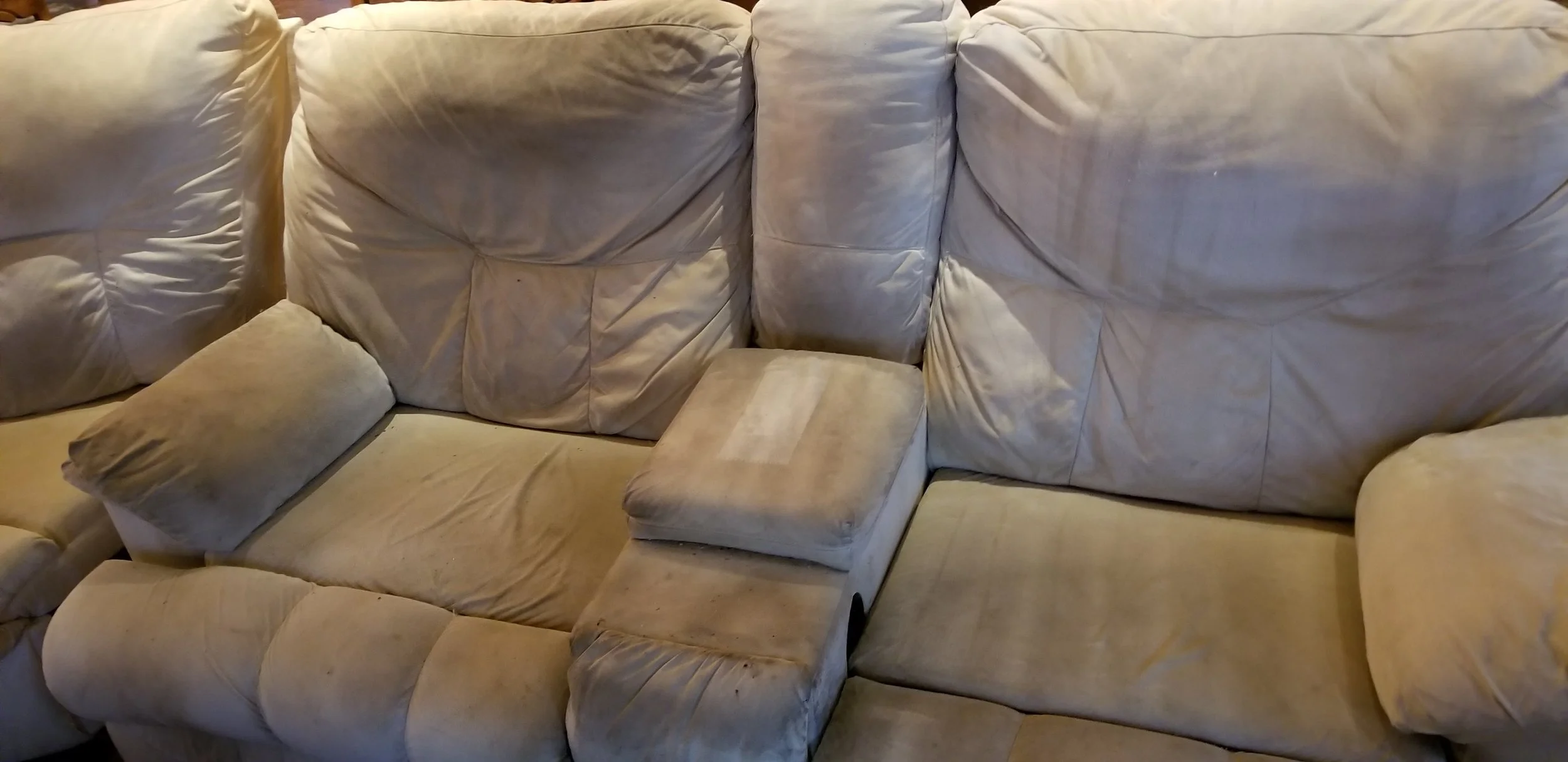 A beige sectional sofa with a built-in ottoman in the center, showing parts of mismatched cushions and visible fabric stains.
