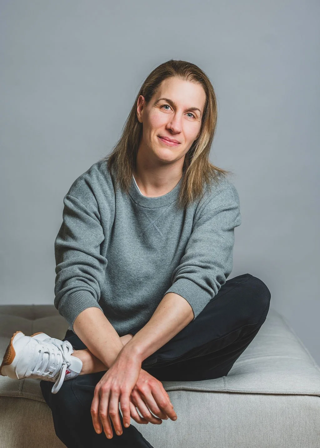 Une femme physiothérapeute à Sherbrooke est assise sur un canapé gris et elle regarde vers l'objectif avec un sourire sympathique.
