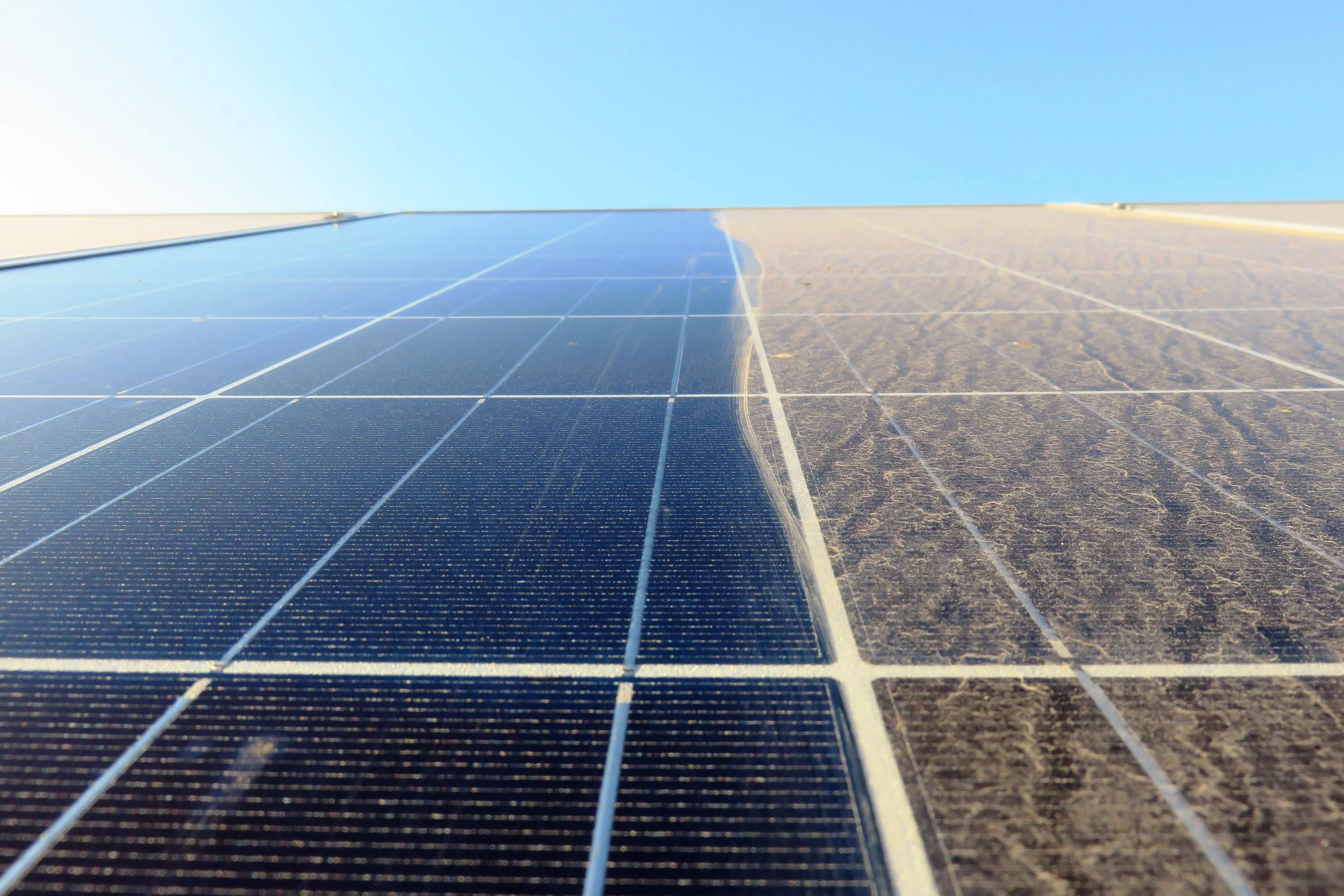 Close-up of a solar panel on a roof, with part of the panels in shadow and part in sunlight, under a clear blue sky.