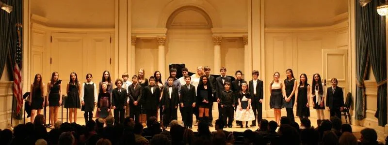 A choir of children and teenagers on stage in a formal setting, with a conductor in front, performing in front of an audience.