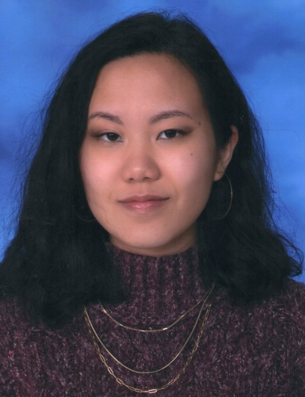 Young woman with black, shoulder-length hair, wearing hoop earrings, layered gold necklaces, and a maroon turtleneck sweater, against a blue background.