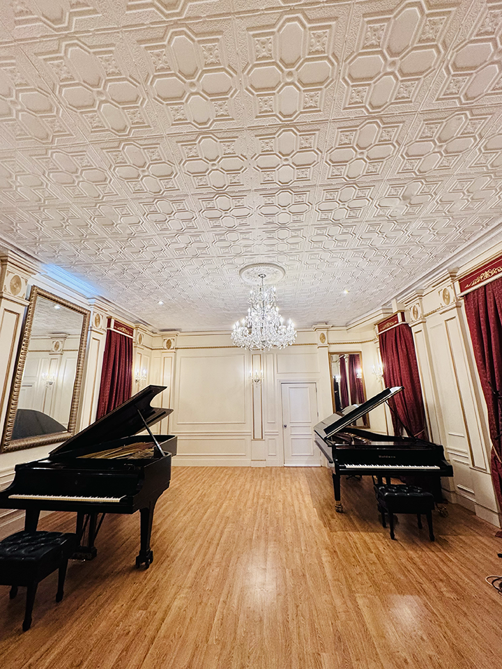 Two grand pianos in an elegant, ornate room with a chandelier, gold-framed mirror, red curtains, and wood flooring.