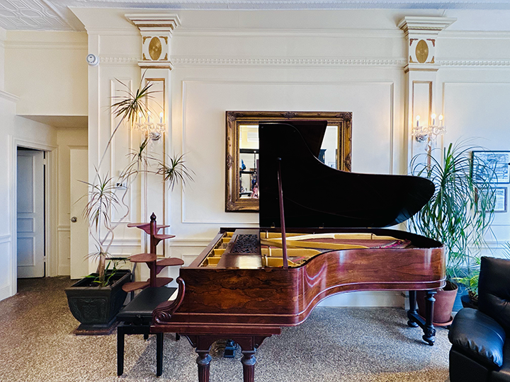 A grand piano in a decorated room with plants, a mirror, and wall-mounted lights.