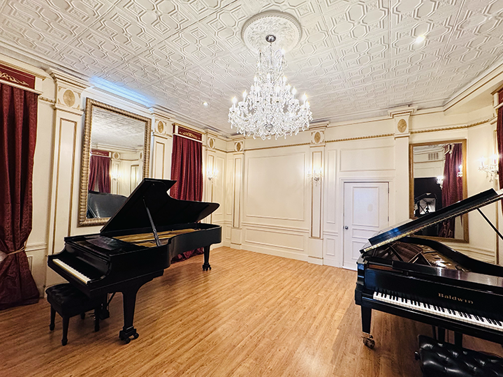 Elegant music room with two grand pianos, ornate ceiling, chandelier, mirrors, and red curtain drapes.