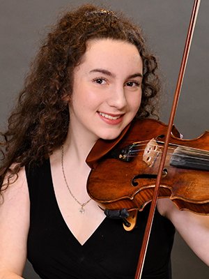 Young woman with curly hair playing a violin and smiling at the camera.