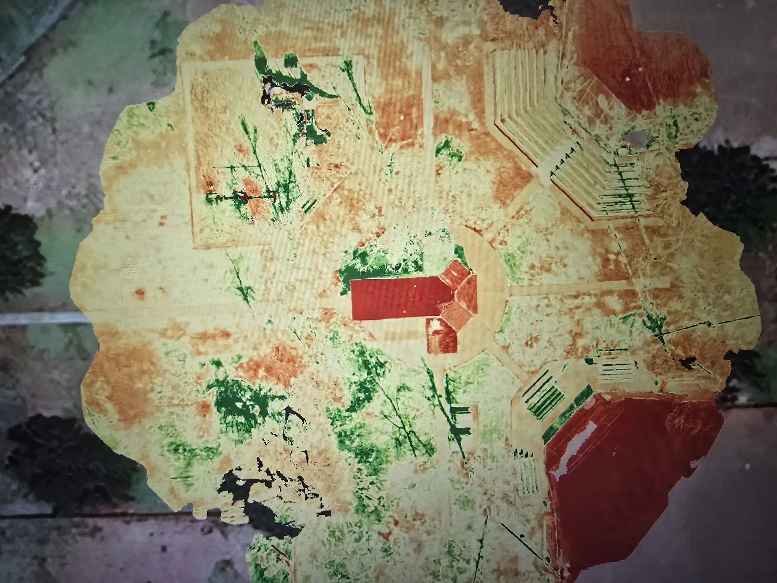 Aerial view of agricultural fields and a large red-roofed building surrounded by trees.