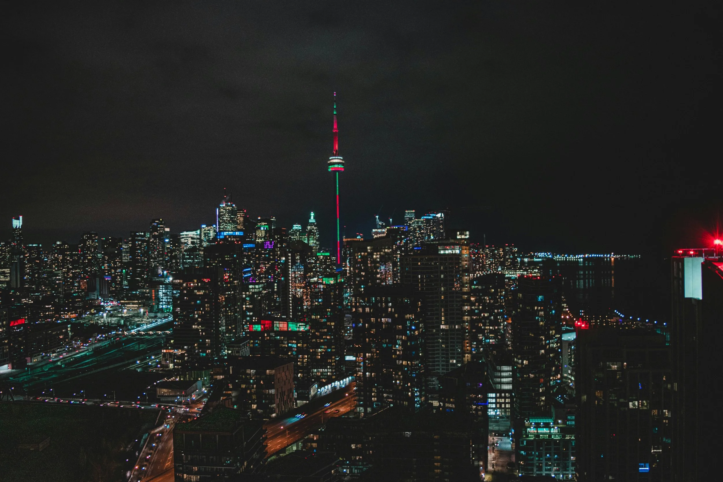 Nighttime city skyline with tall illuminated skyscrapers and a prominent tower with colorful lights.