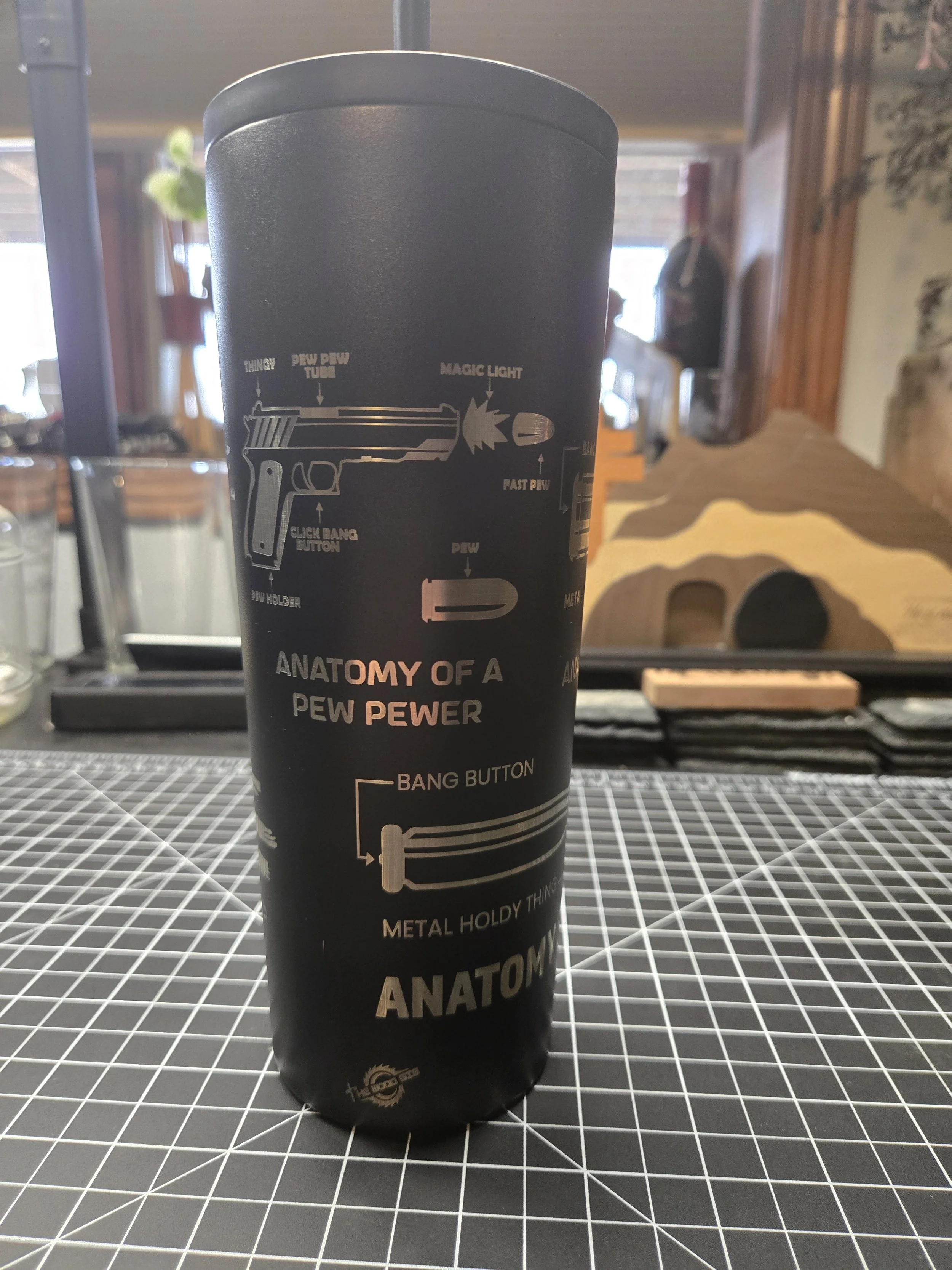 A cylindrical container with diagrammatic illustrations and text explaining the anatomy of a PEW PEW PEW laser gun, including parts like the trigger, barrel, and button, in black and white with orange accents.