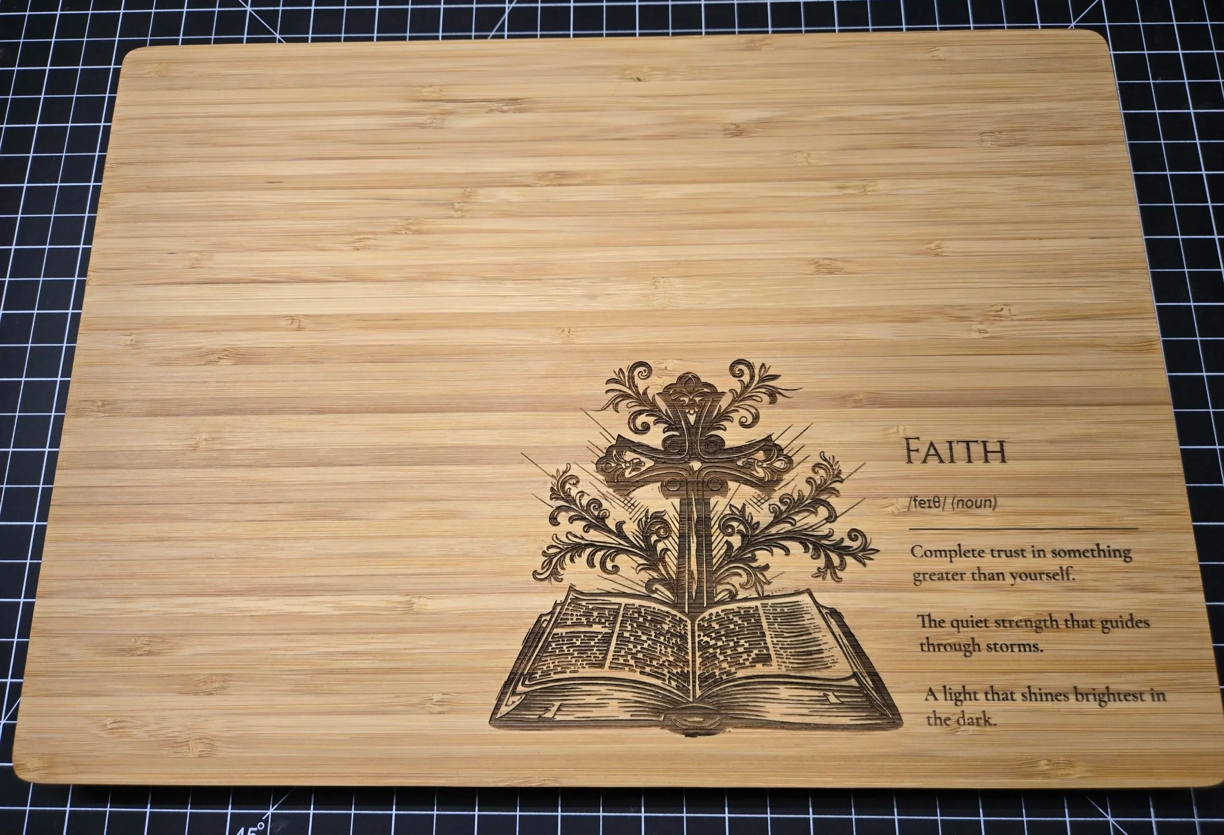 A wooden cutting board with an engraved design featuring an open book, a cross, decorative floral elements, and the word 'FAITH' with its definition and related quotes.