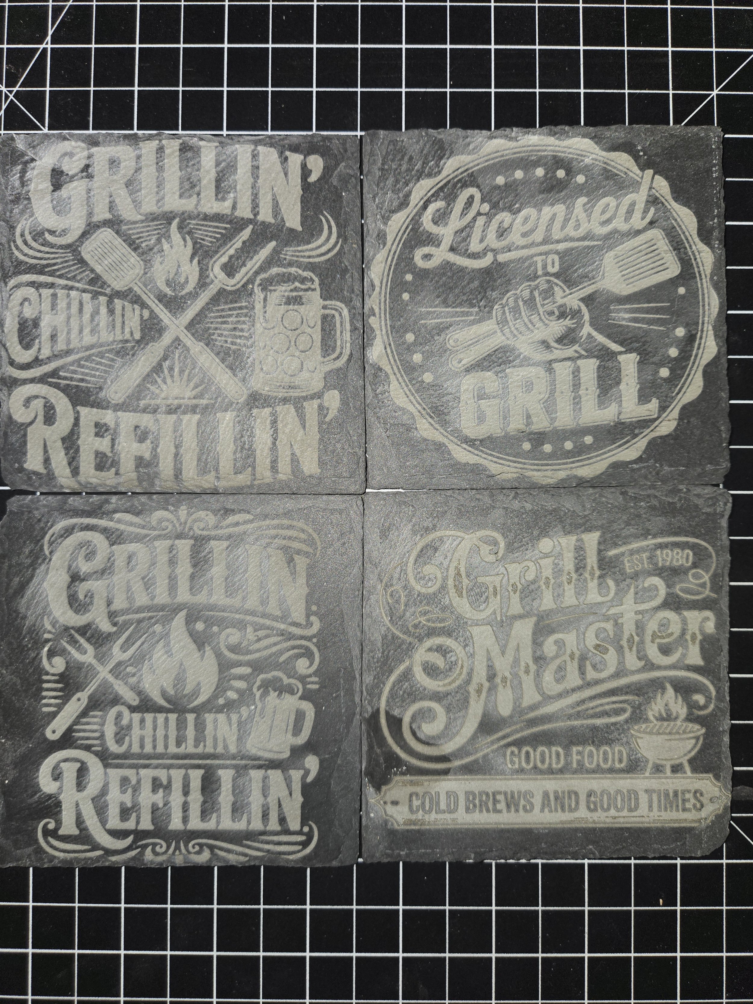 Four gray stone coasters with white printed designs and text related to grilling and barbecues.