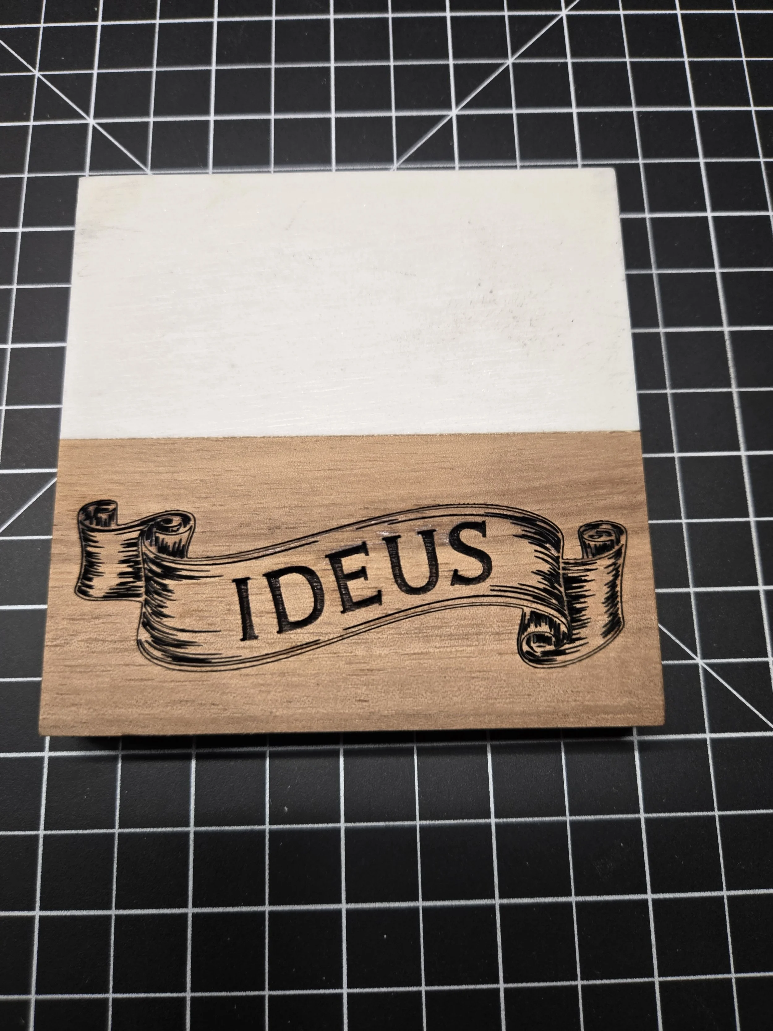 Wooden stamp with the word "IDEUS" on a black grid cutting mat.