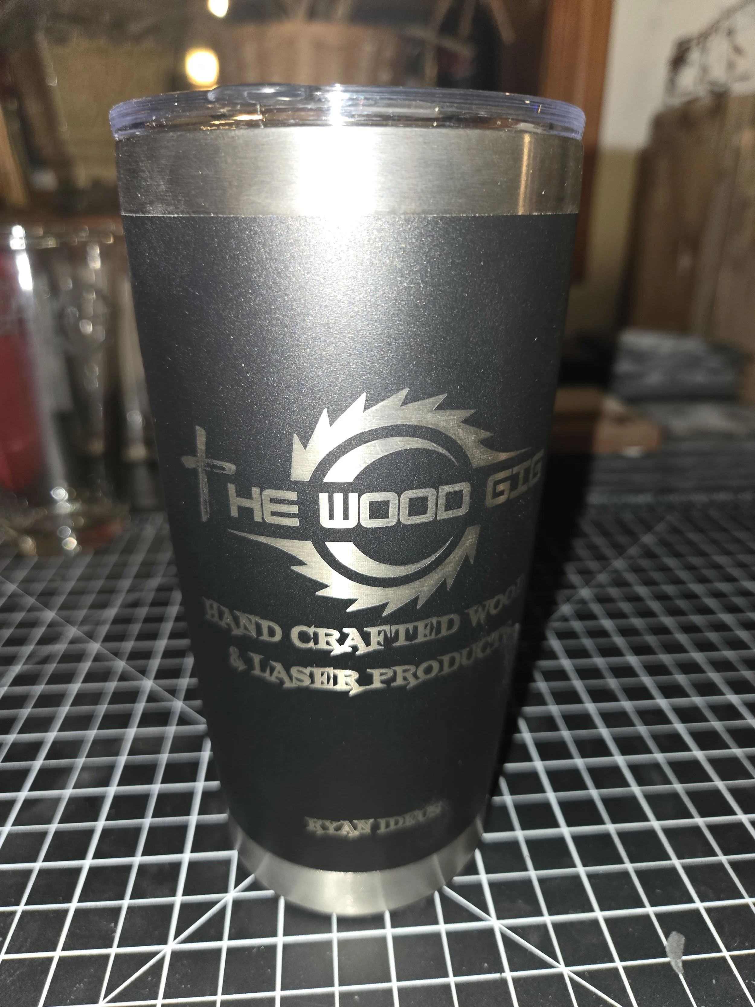 A black travel tumbler with stainless steel accents and logo that reads "The Wood Stick" and "Hand Crafted Wooden & Laser Products."