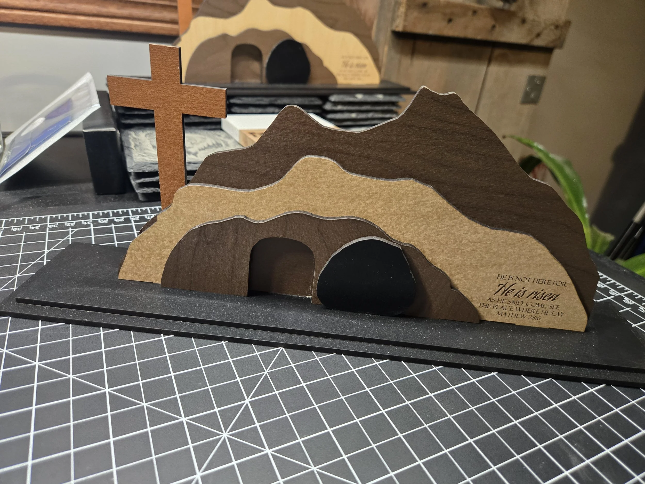 Wooden display featuring mountain silhouette with a cross on the left side and an inscription on the right side, placed on a black base.