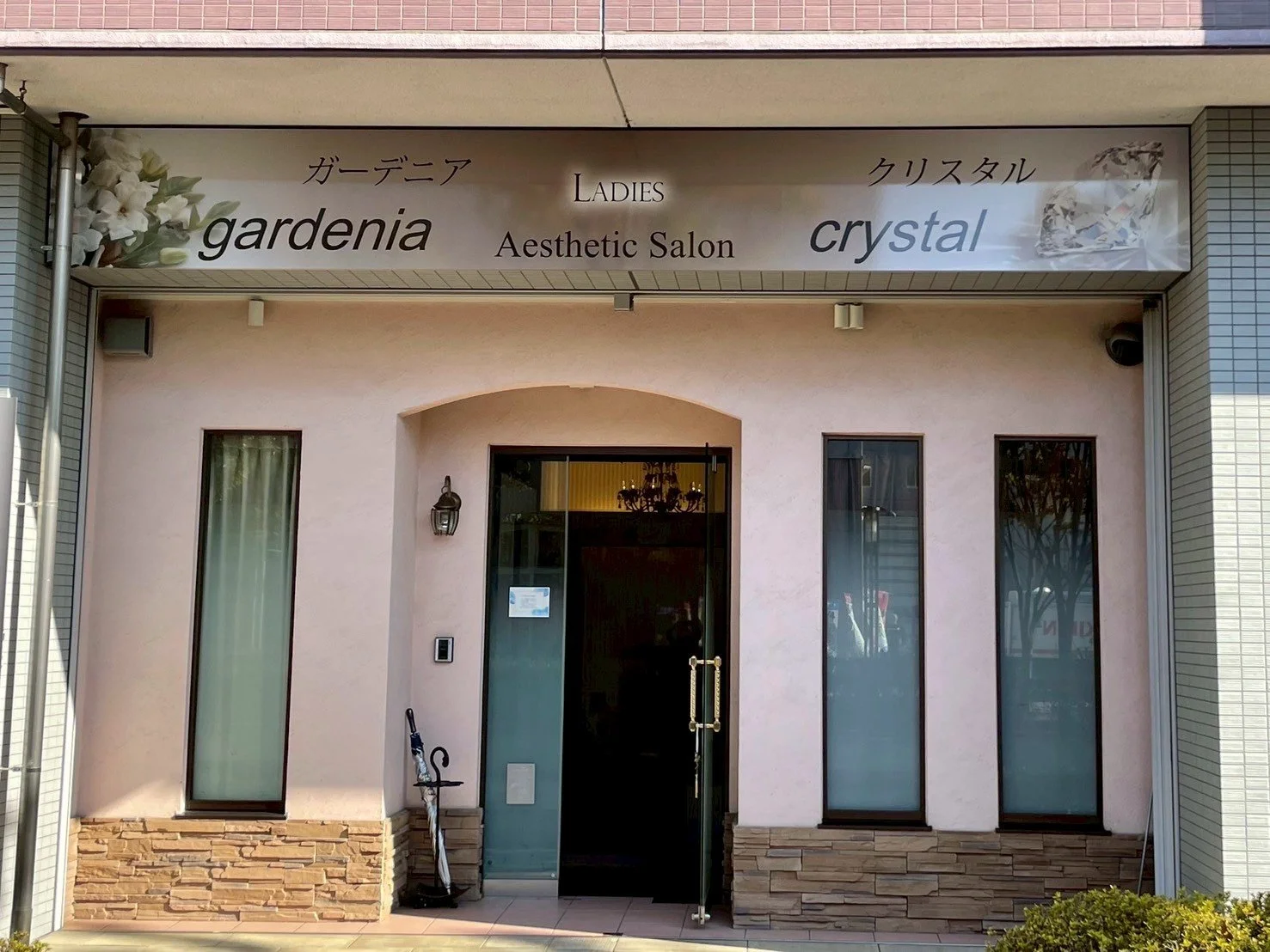 美容サロンの入口と看板。看板には「ガーデニア」「クリスタル」「LADIES Aesthetic Salon」などの文字と花の画像。