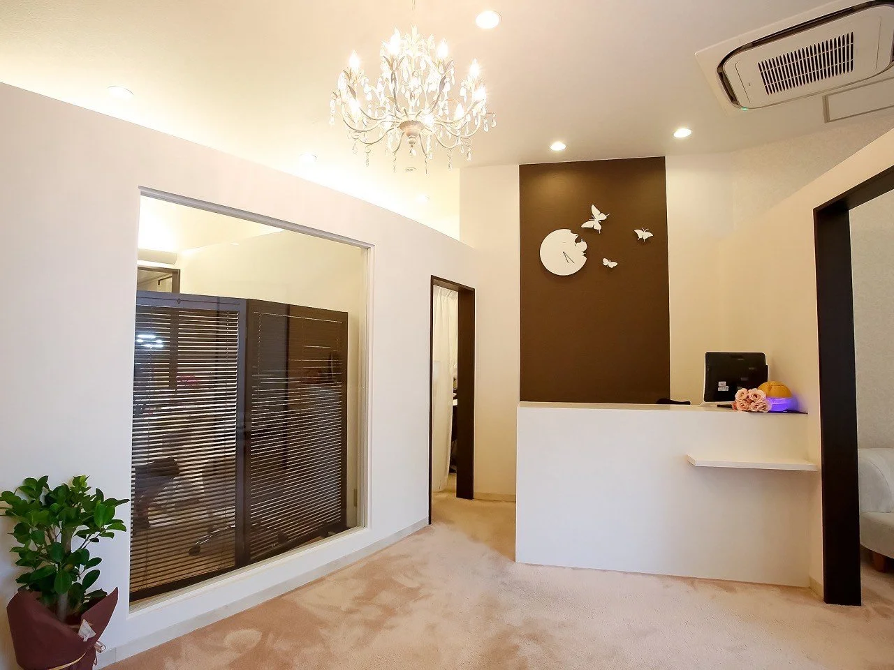 受付カウンターと壁に時計と蝶の飾り、エアコンと観葉植物。