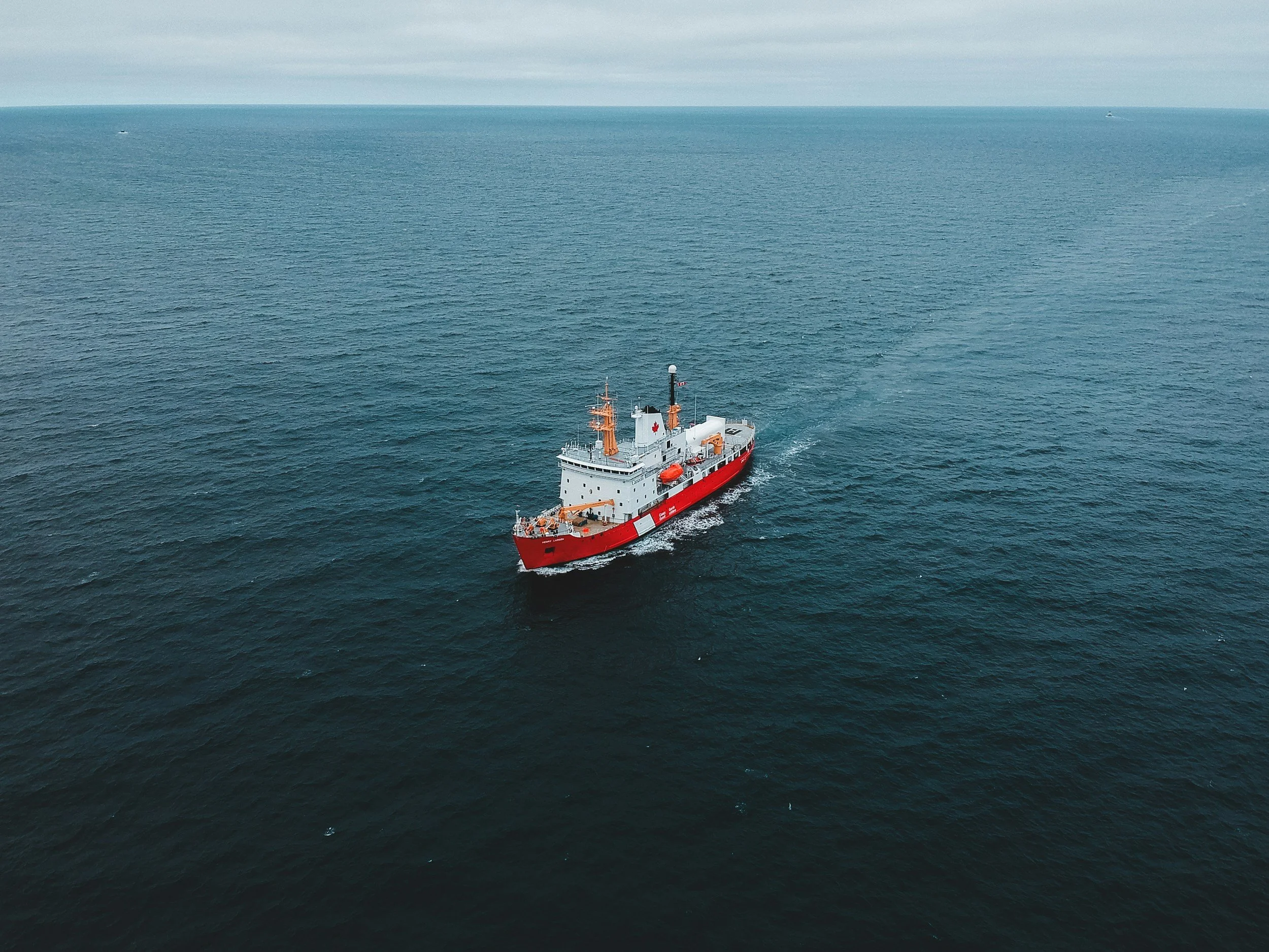 A large red and white ship sailing on the ocean with a cloudy sky overhead.