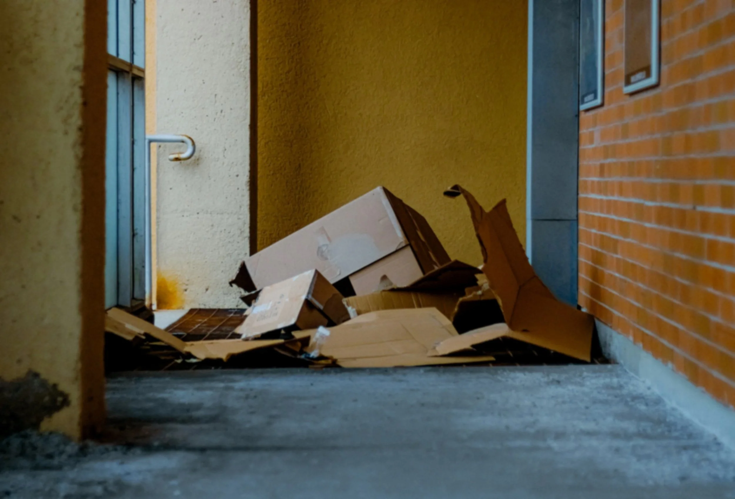 View from the ground showing a doorway with a metal frame, yellow wall, and scattered cardboard boxes on a brick floor.