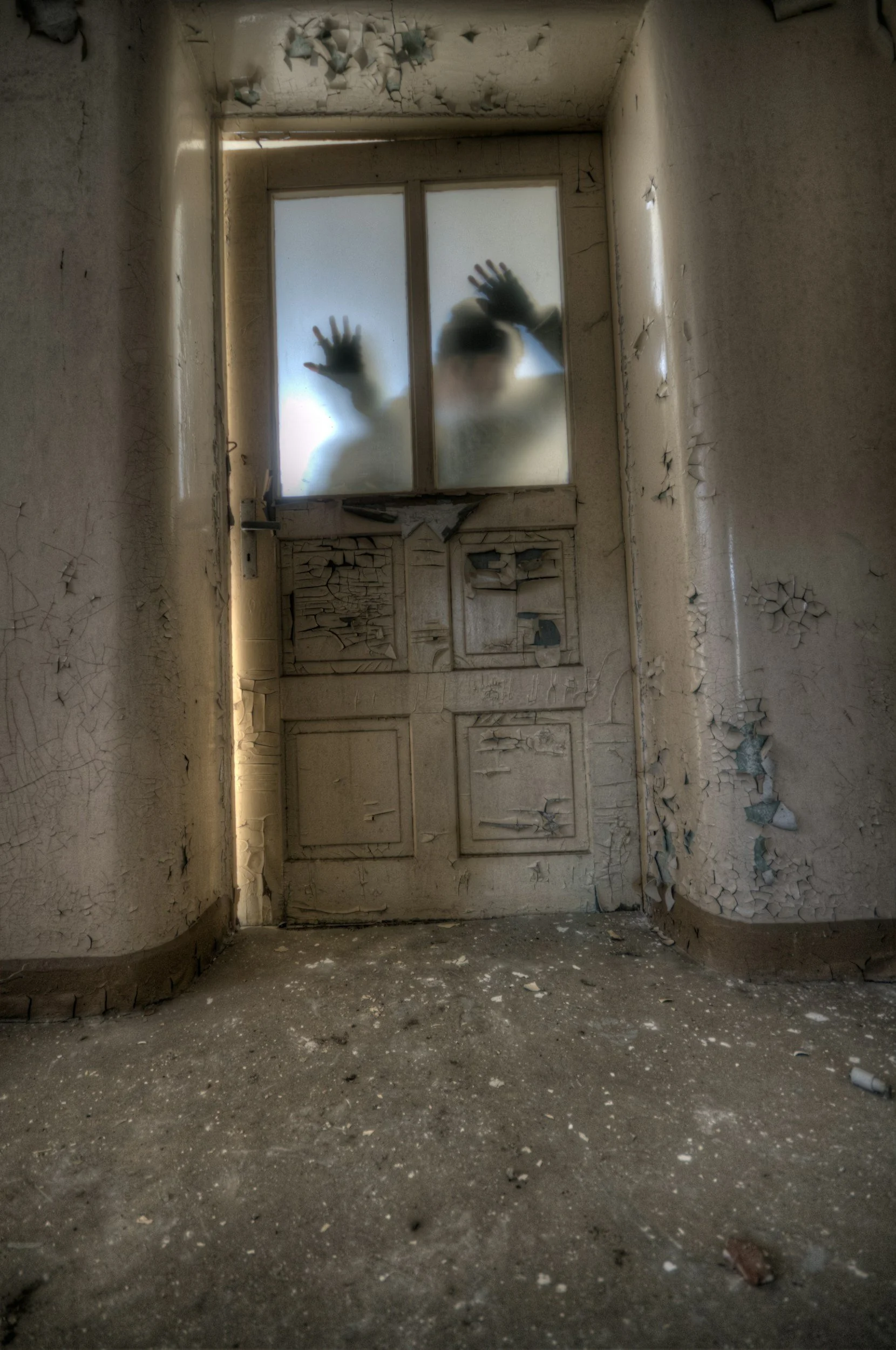 Silhouettes of two children pressing their hands and faces against a foggy, dirty window in an abandoned, deteriorated room with peeling paint and cracked walls.