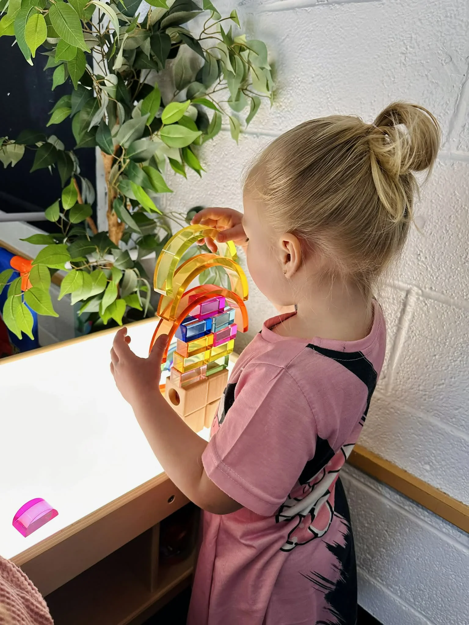 Child standing, playing with a light table and building with clear colorful blocks.