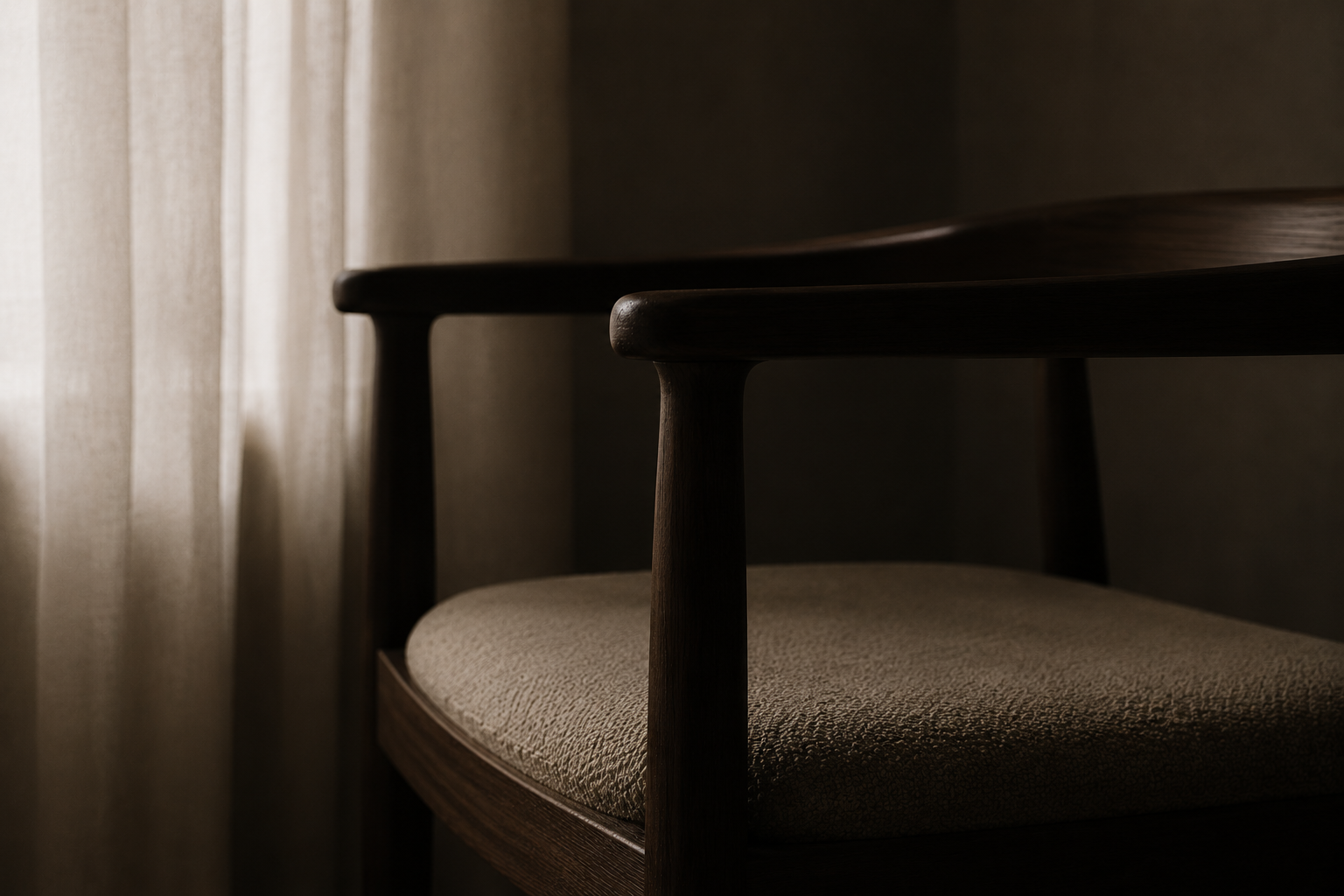 A wooden chair with beige cushion near a window with light-colored curtains, in low lighting.