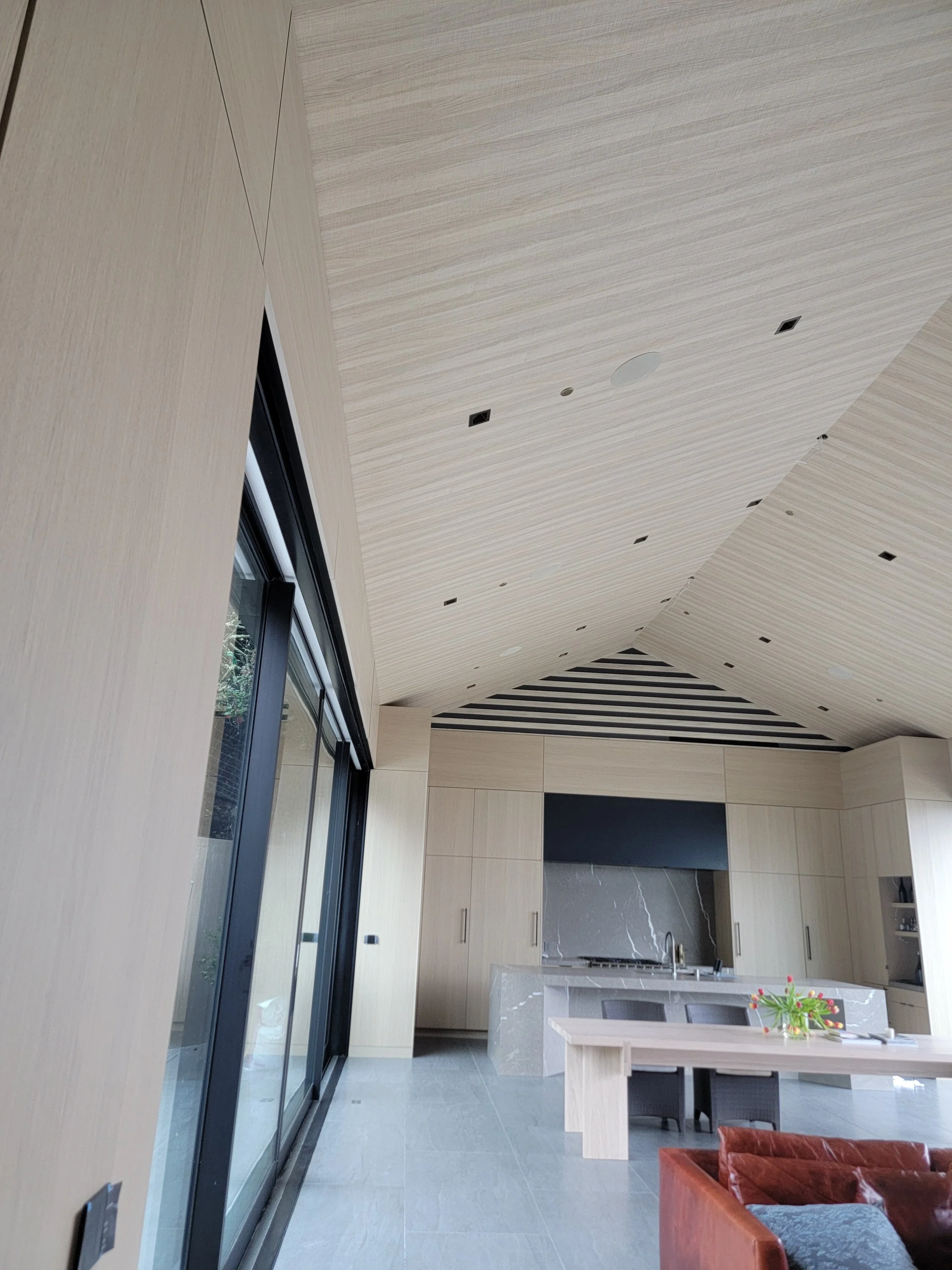 Modern kitchen with light wood cabinets, marble island, and a large sliding glass door leading outside.