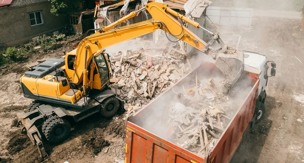 A yellow excavator loading debris into a red dump truck during demolition work.