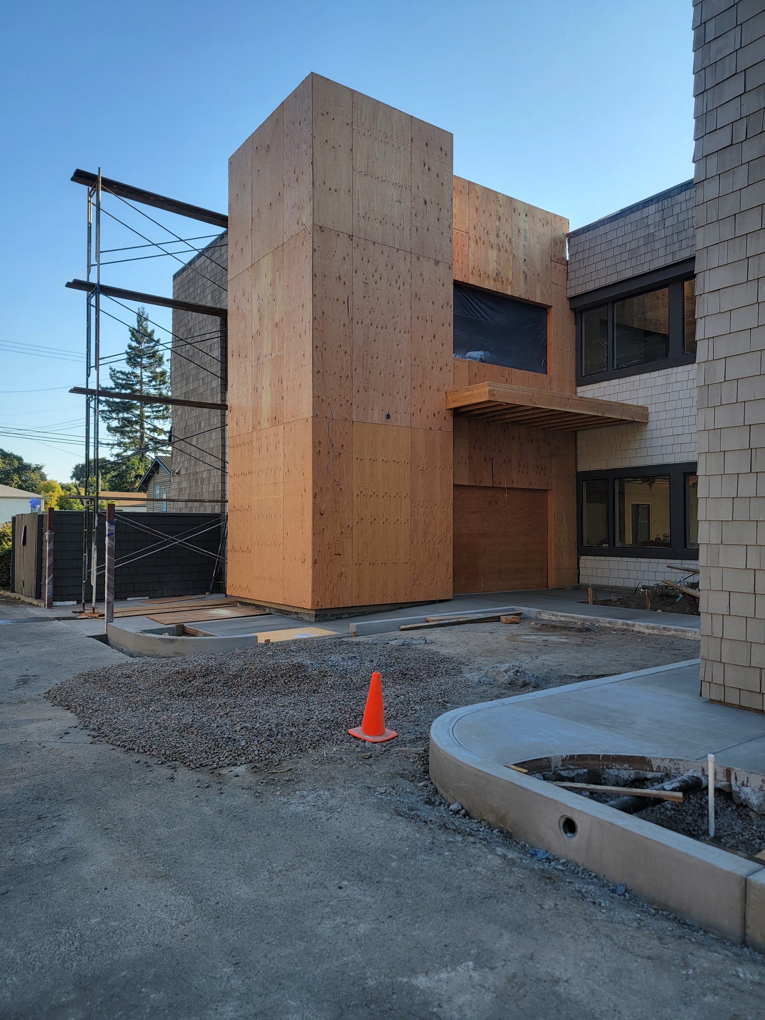 Construction site with a new building being built; wooden exterior walls and scaffolding on the left side; orange traffic cone in front.