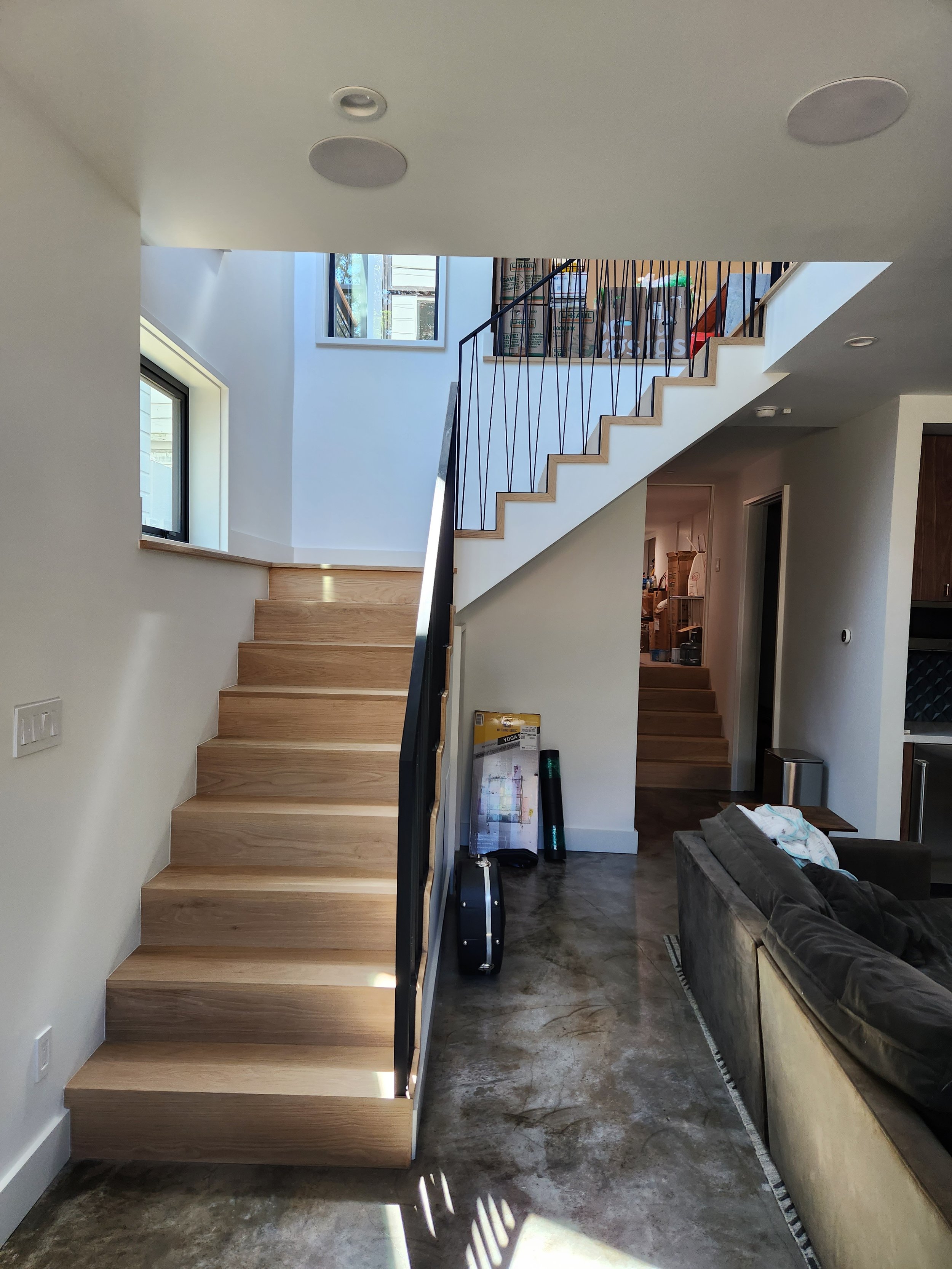 Interior view of a modern home with a wooden staircase, white walls, large windows, and concrete flooring.