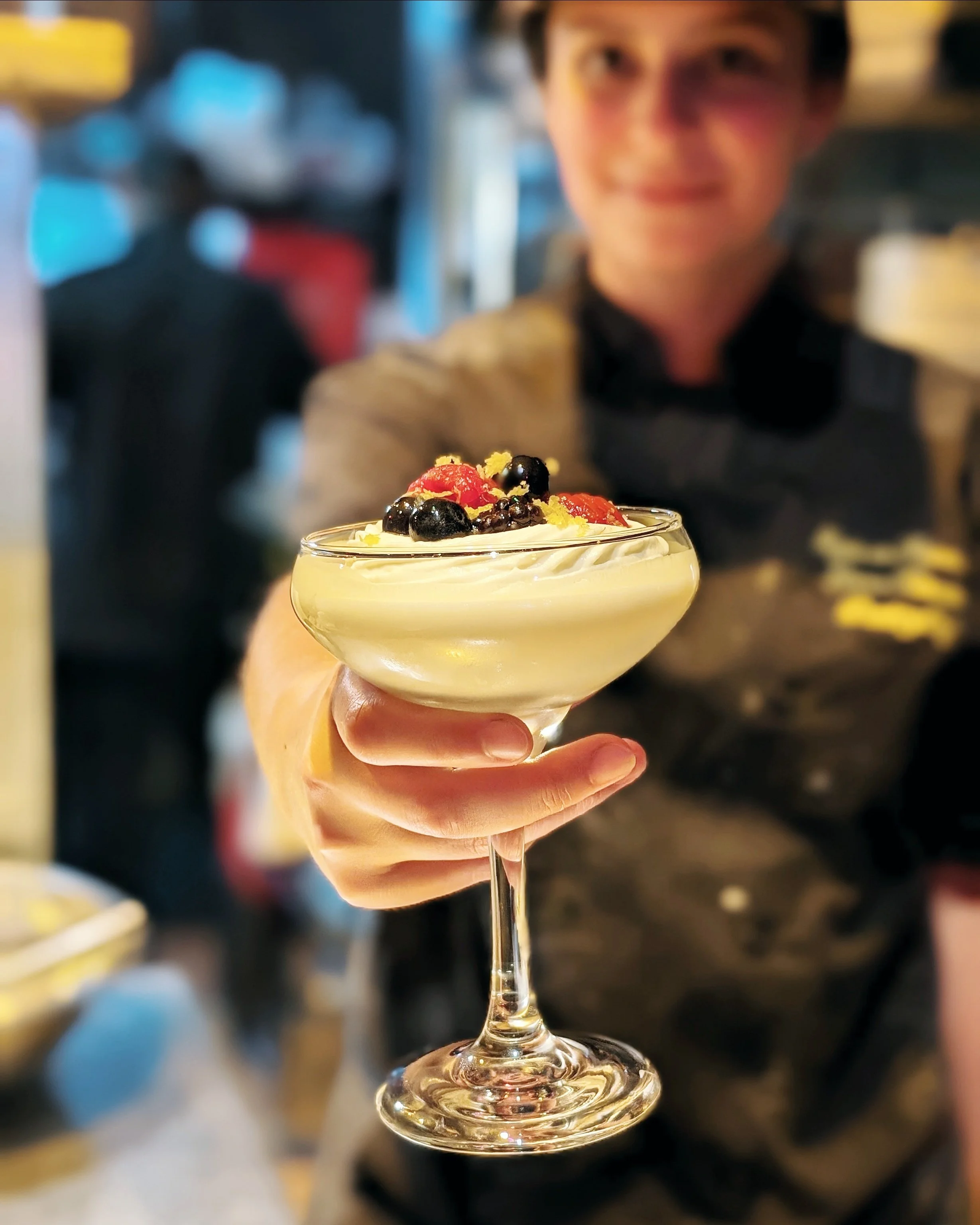 A person holding a glass of dessert topped with berries and lemon zest.