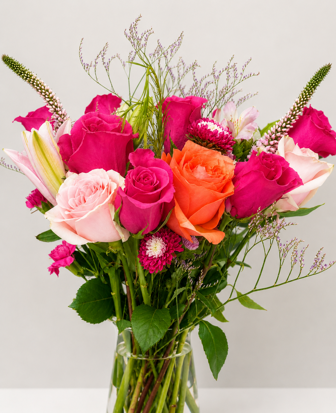 Romantic floral arrangement featuring pink, coral, and red roses with delicate seasonal flowers and greenery.