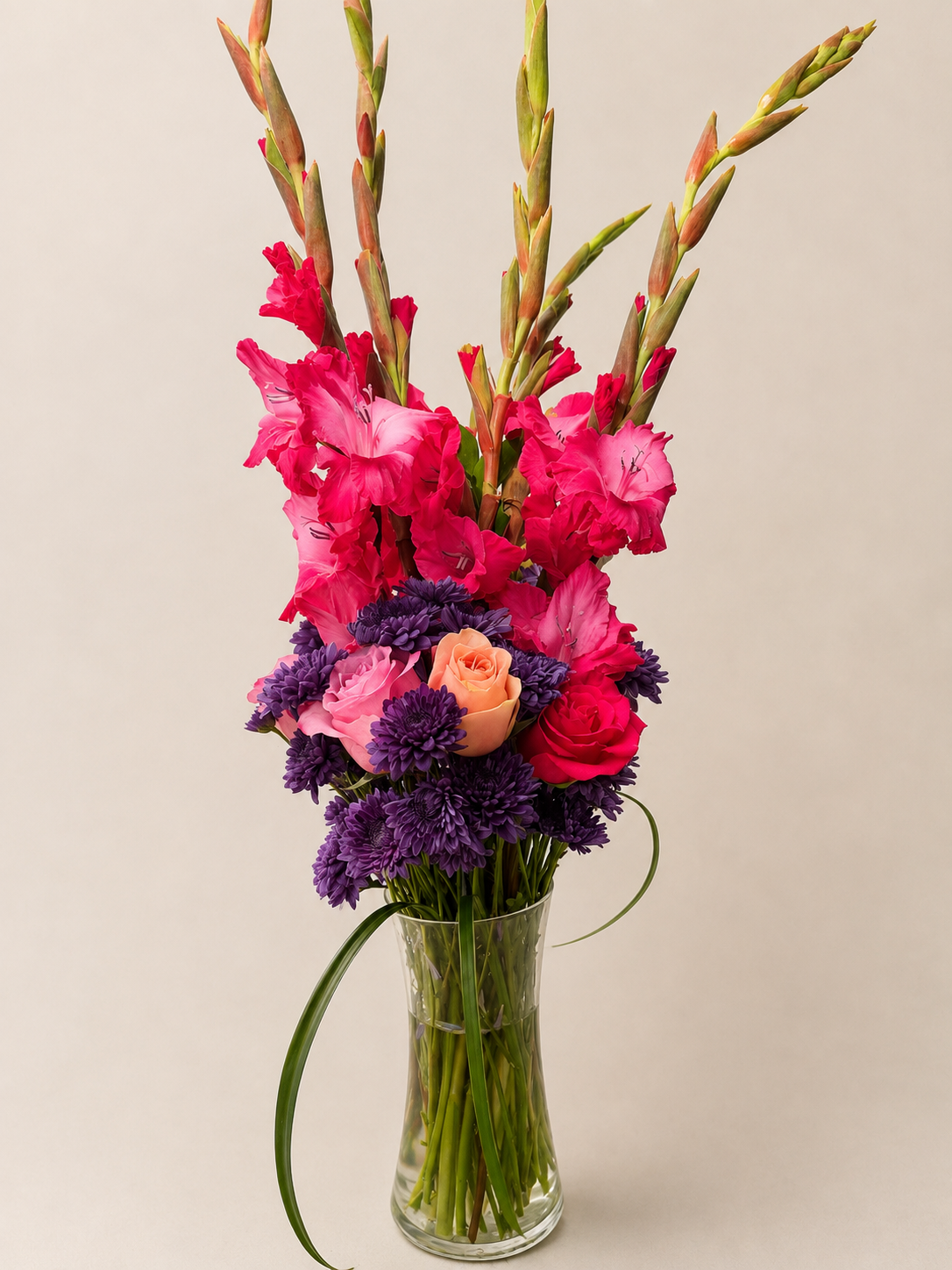 Tall custom floral arrangement featuring vivid pink gladiolus, deep purple chrysanthemums, and pink and peach roses.